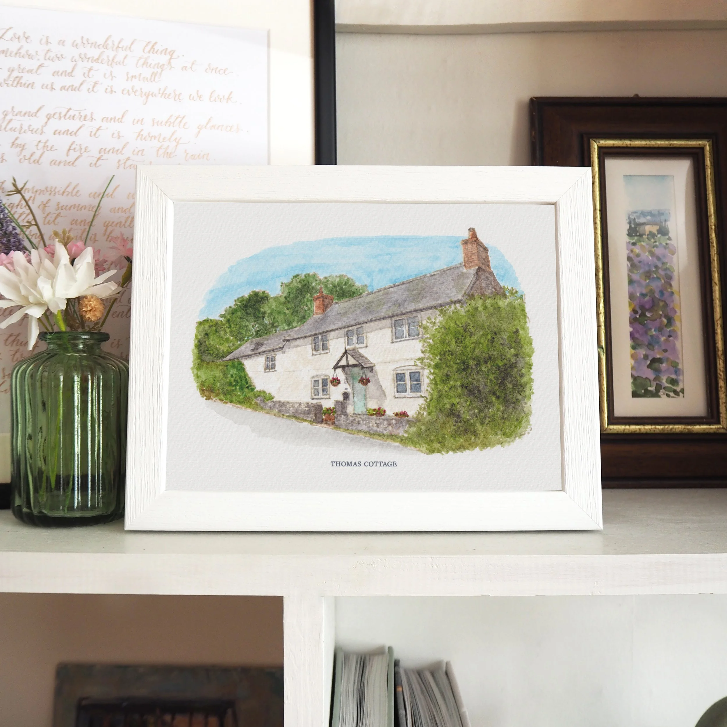 A framed watercolour house portrait of a white cottage