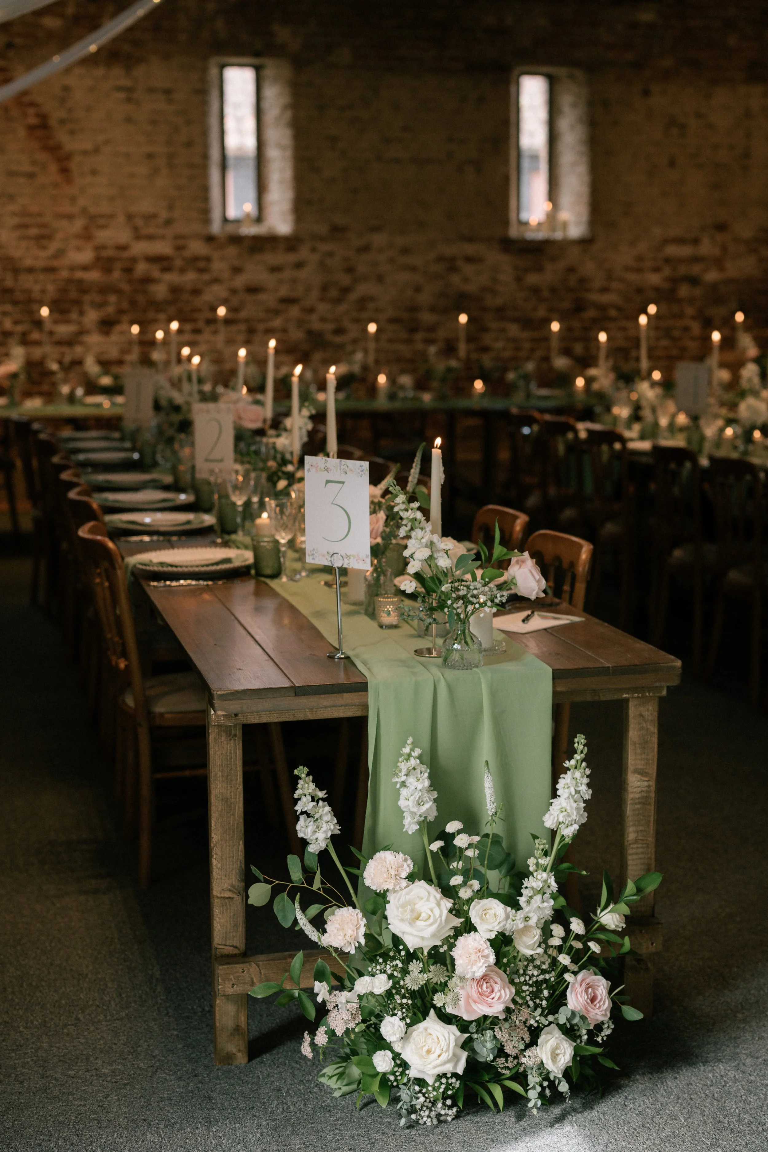 a rustic wedding table set up with green draping, pink and white flowers and table numbers. Image by Laura Williams Photography.
