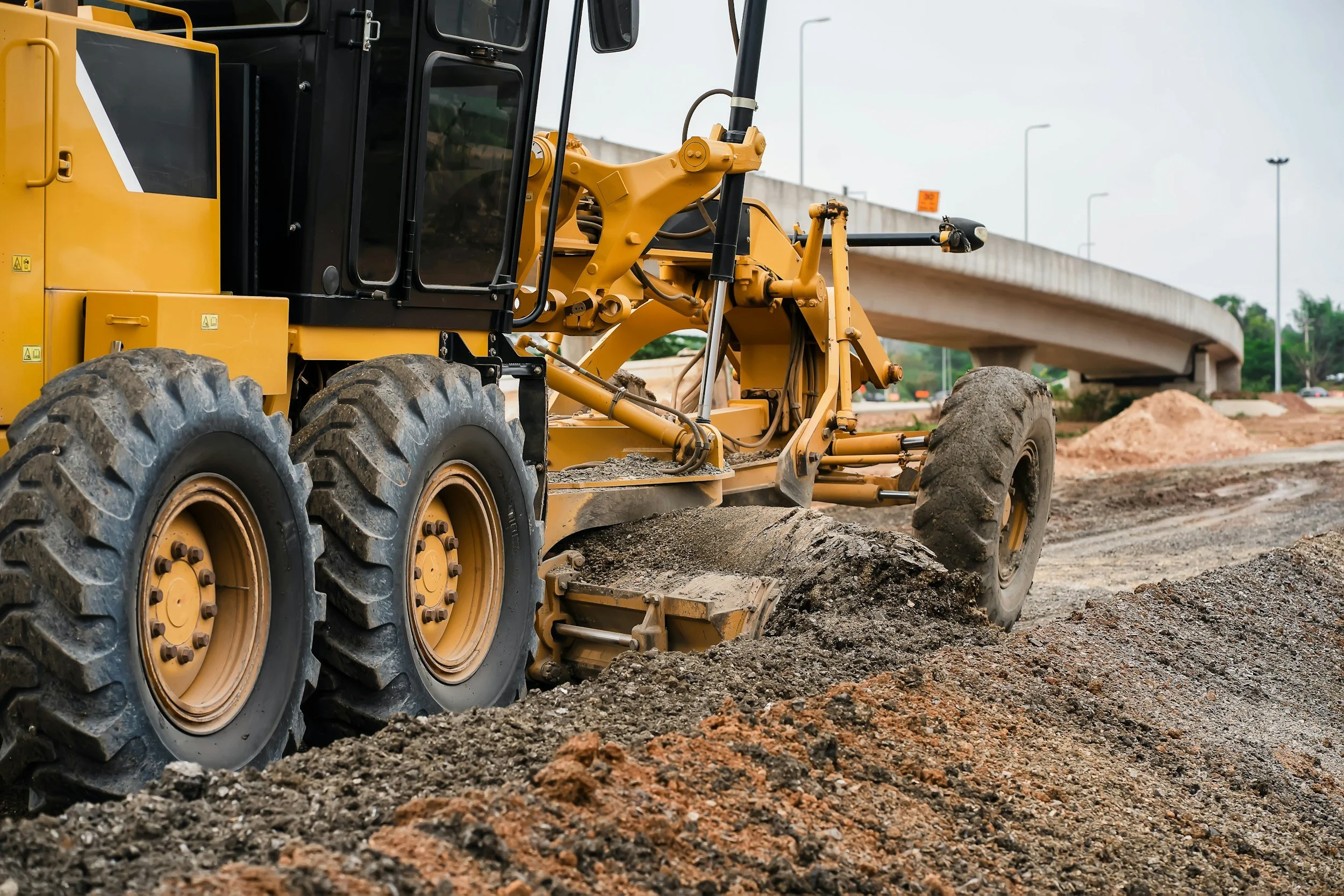 Road grader spreading and leveling loose road material during gravel road preparation.