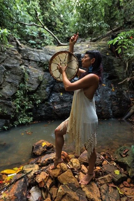 Frau im Wasser, die einen Traumfänger hält und hinter einem Wasserfall im Dschungel steht.