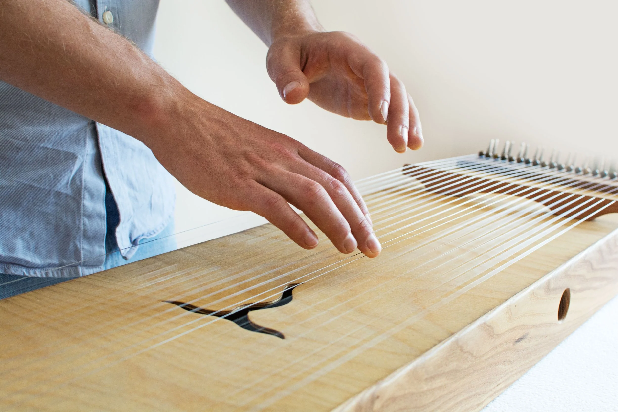 Nahaufnahme von Händen, die eine Zither spielen, auf einem Holztisch.