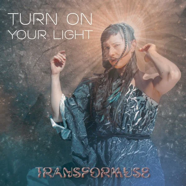 Ayam with wet hair, wearing a patterned dress, standing in front of a textured background with sunlight shining behind her. The title of the Single on the image reads 'TURN ON YOUR LIGHT' at the top