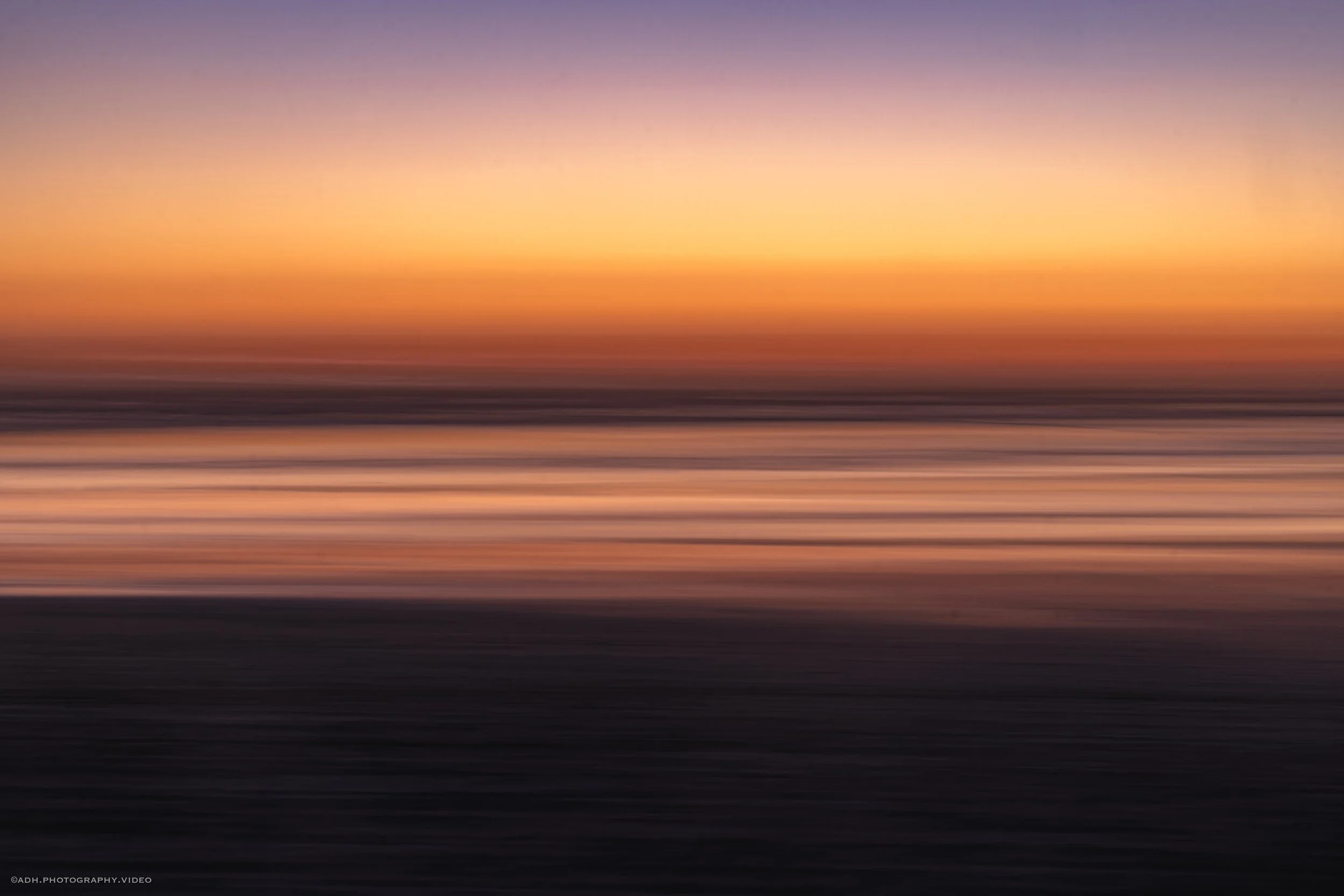 Blurred image of a sunset over the ocean with vibrant orange, pink, purple, and dark blue colors, and rippling water.