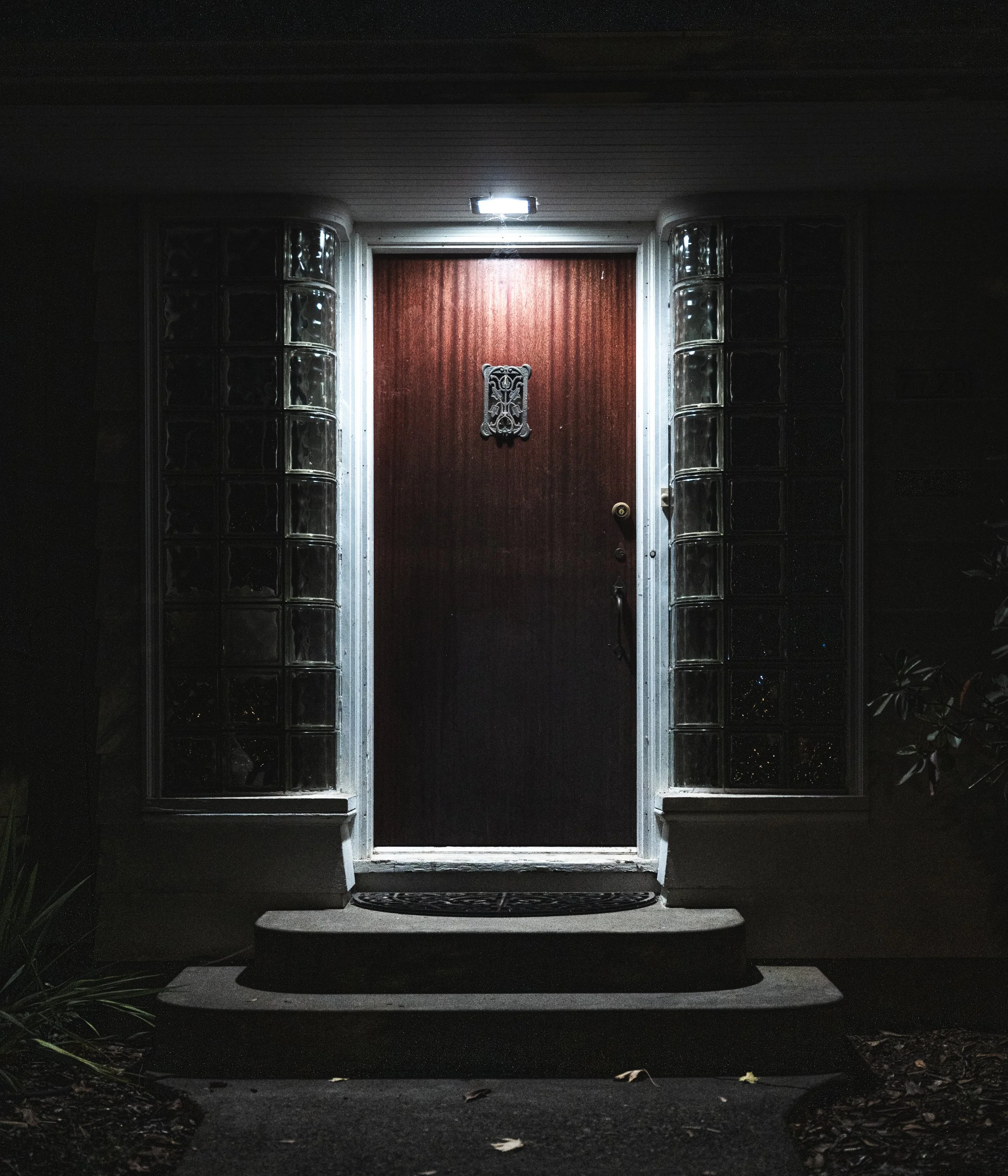 Front door illuminated at night, with glass block sides and a decorative metal house number plaque.