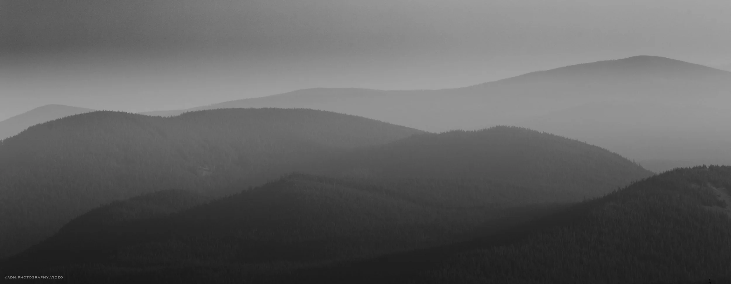 Black and white photograph of multiple mountain ridges with mist or fog in the valleys between them.