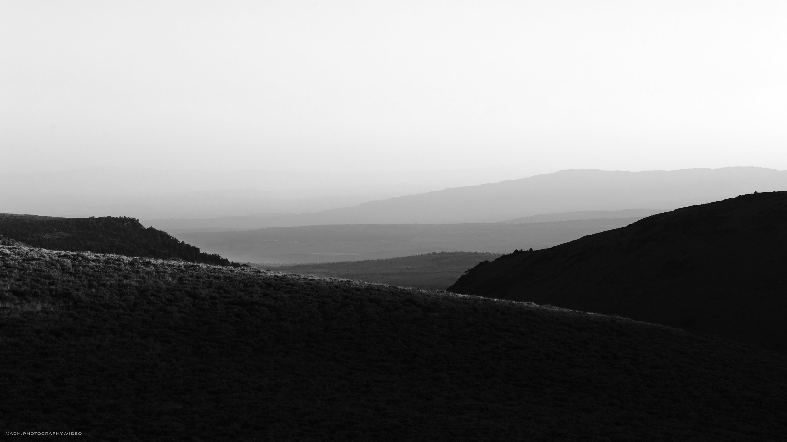 Black and white photo of layered rolling hills or mountains with a misty or foggy background.