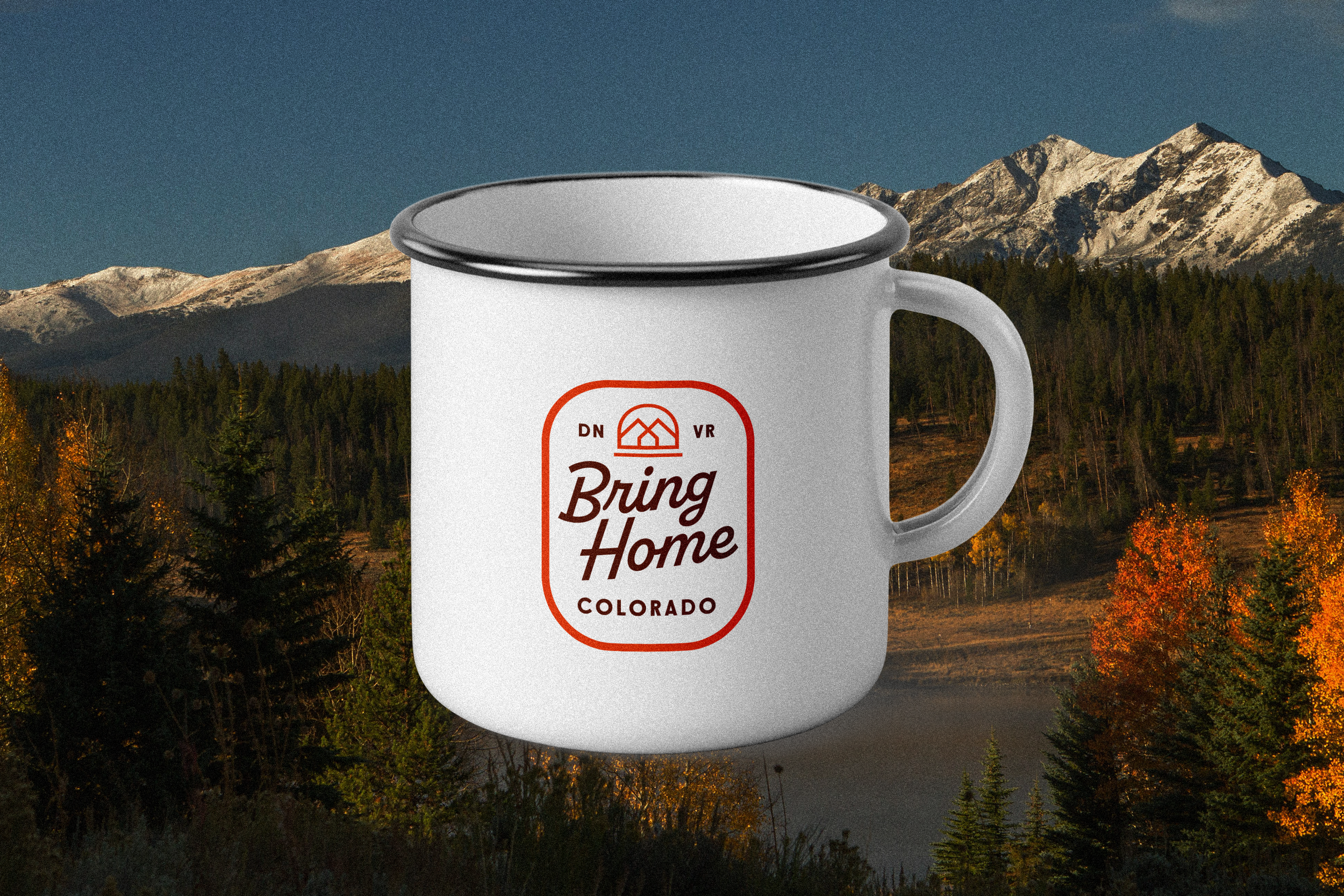 White mug with red and black text and logo, set against a mountainous forest landscape with autumn trees.