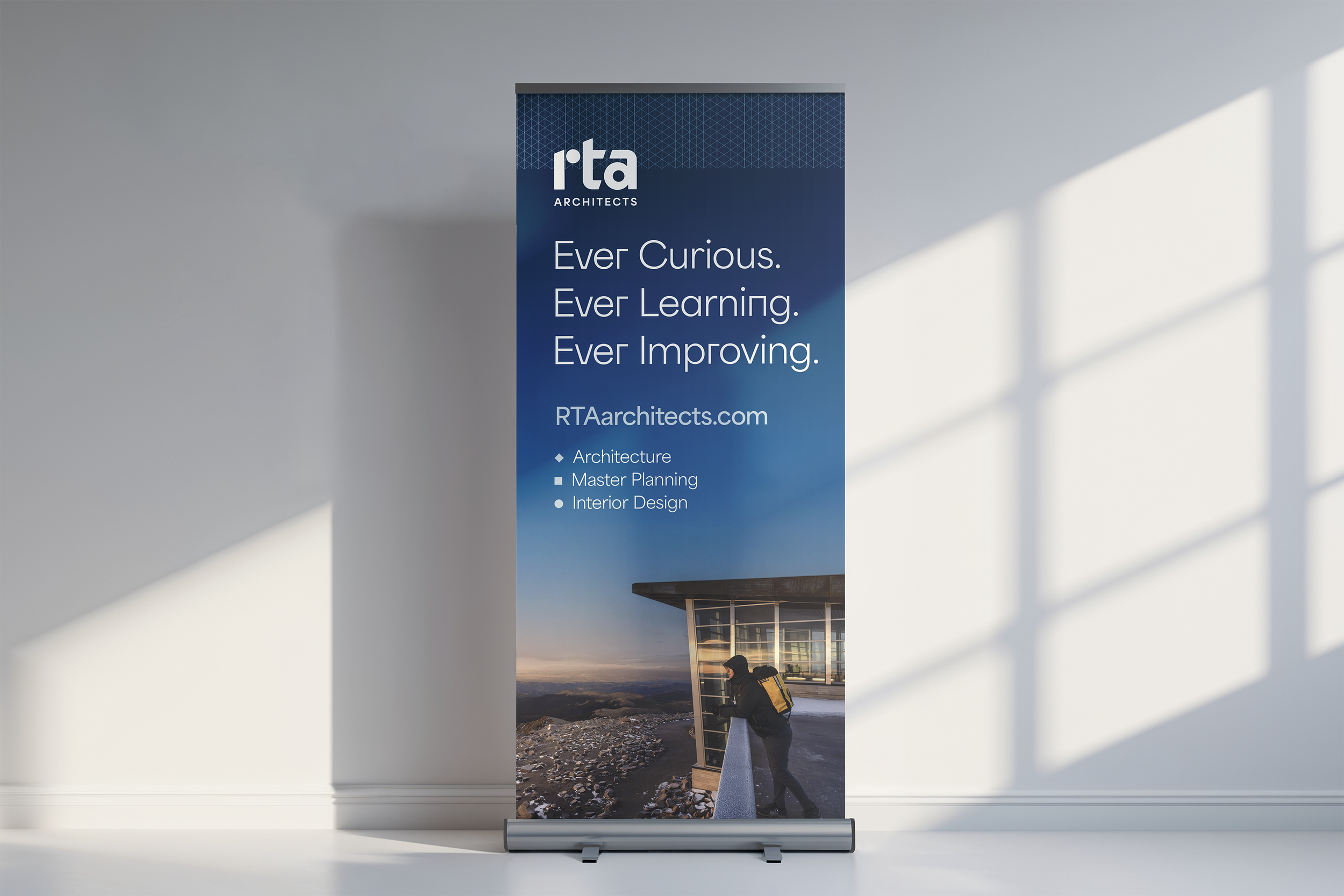A professional vertical banner for RTA Architects, displaying the business slogan 'Ever Curious. Ever Learning. Ever Improving.' with a background image of a person with a backpack looking at a modern building on a mountain ridge.