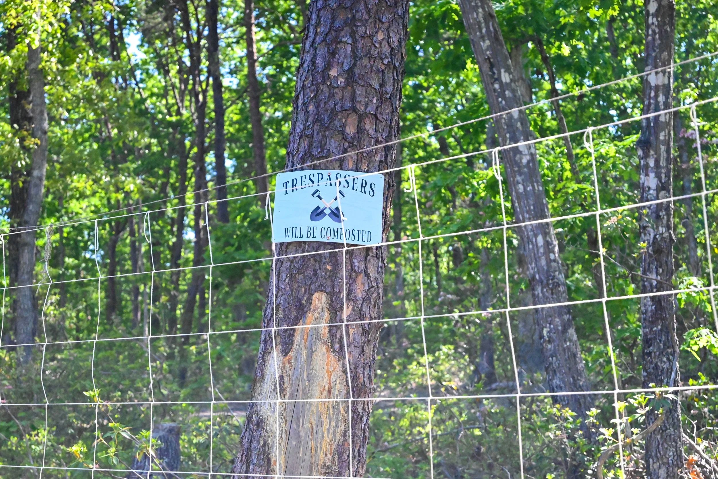 Wooden tree fence with a sign that says 'Trespassers will be composted' in a wooded area.