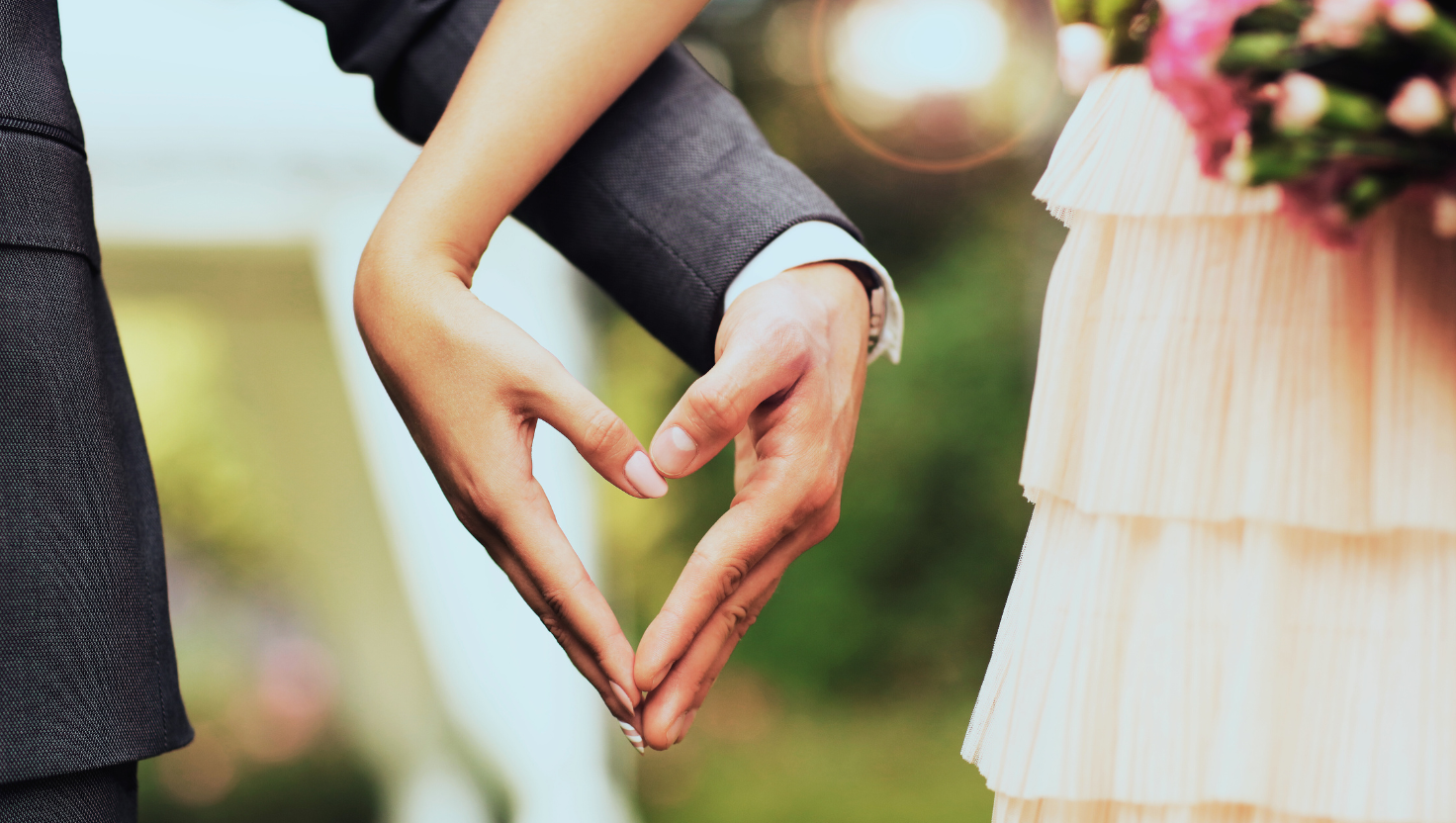 Bride and groom forming heart shape with hands, close-up view.