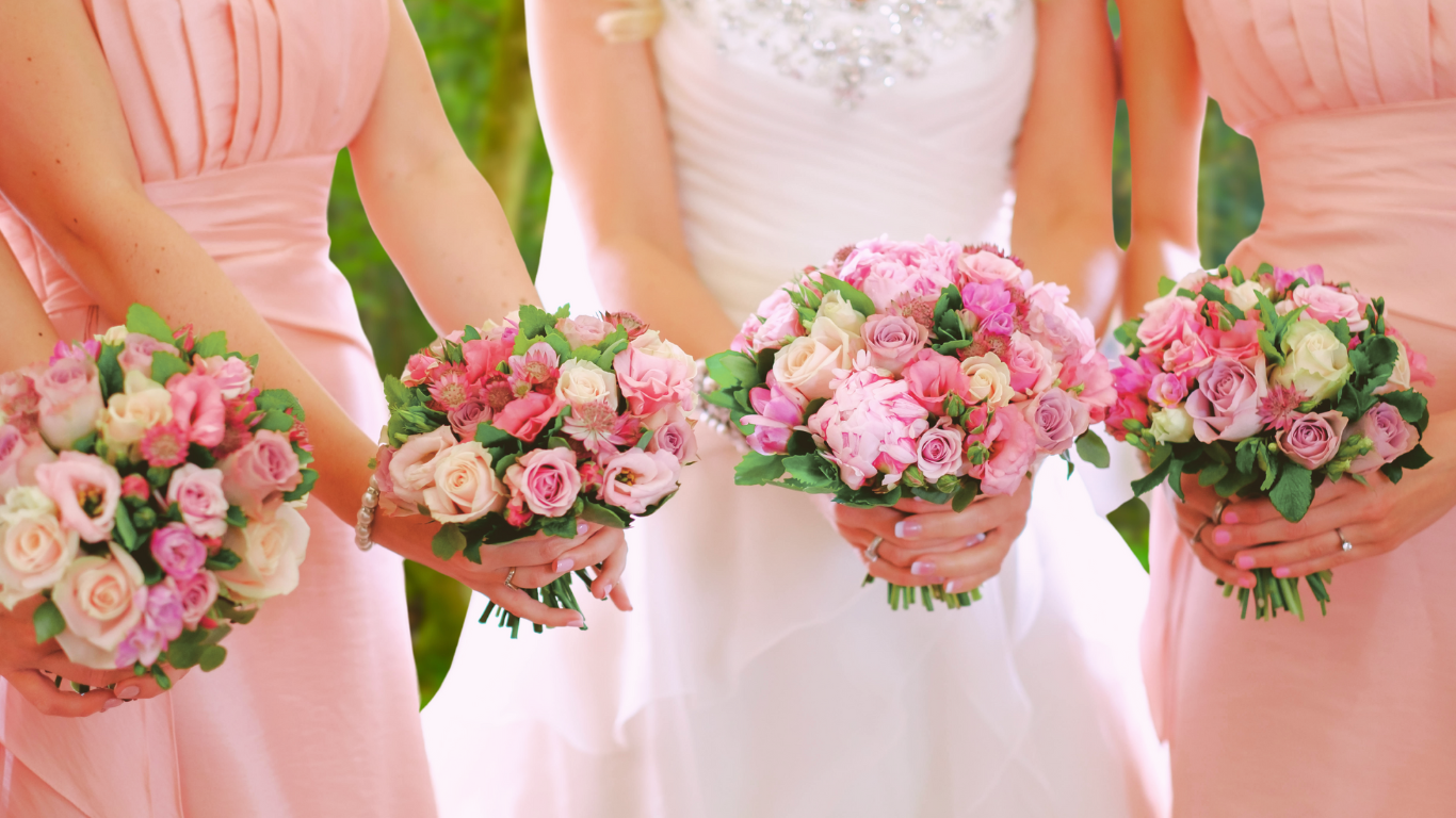 Bridesmaids in pink dresses holding floral bouquets.