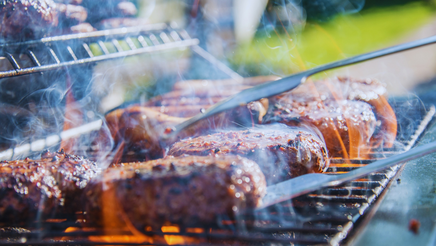 Close-up of steaks grilling on a barbecue with tongs.