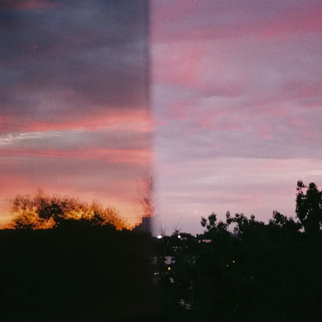A sunset view with pink, purple, and orange clouds, divided in half by a vertical distortion, with trees and city lights visible in the foreground. | The Witch's Therapist | Holistic Psychotherapy in London Ontario