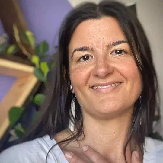 Megan Woods smiles at the camera with long dark hair around her shoulders and her hand placed over her heart | The Witch's Therapist | holistic psychotherapy in London Ontario