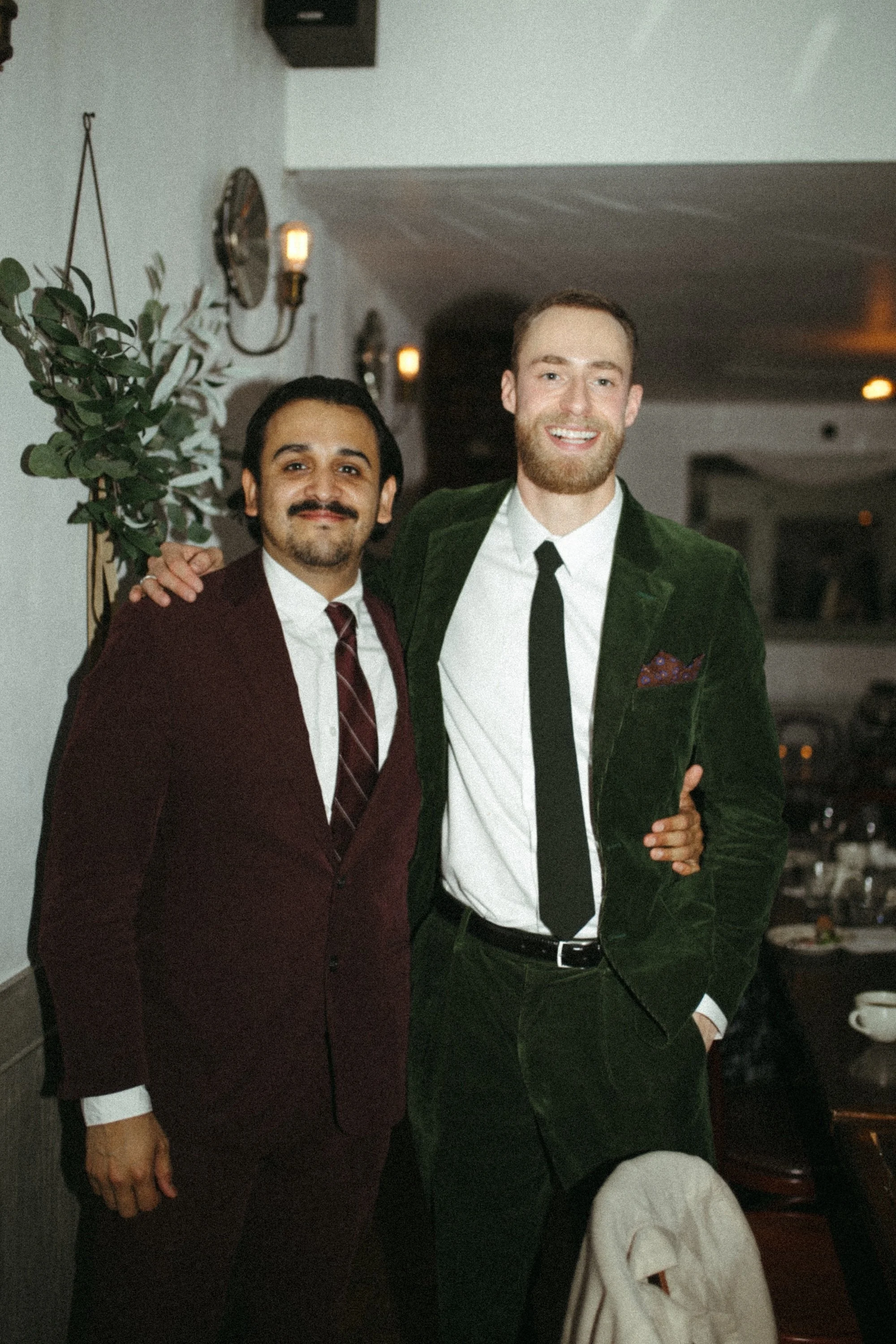 Two GWG colleagues in velvet suits posing arm in arm at dinner.