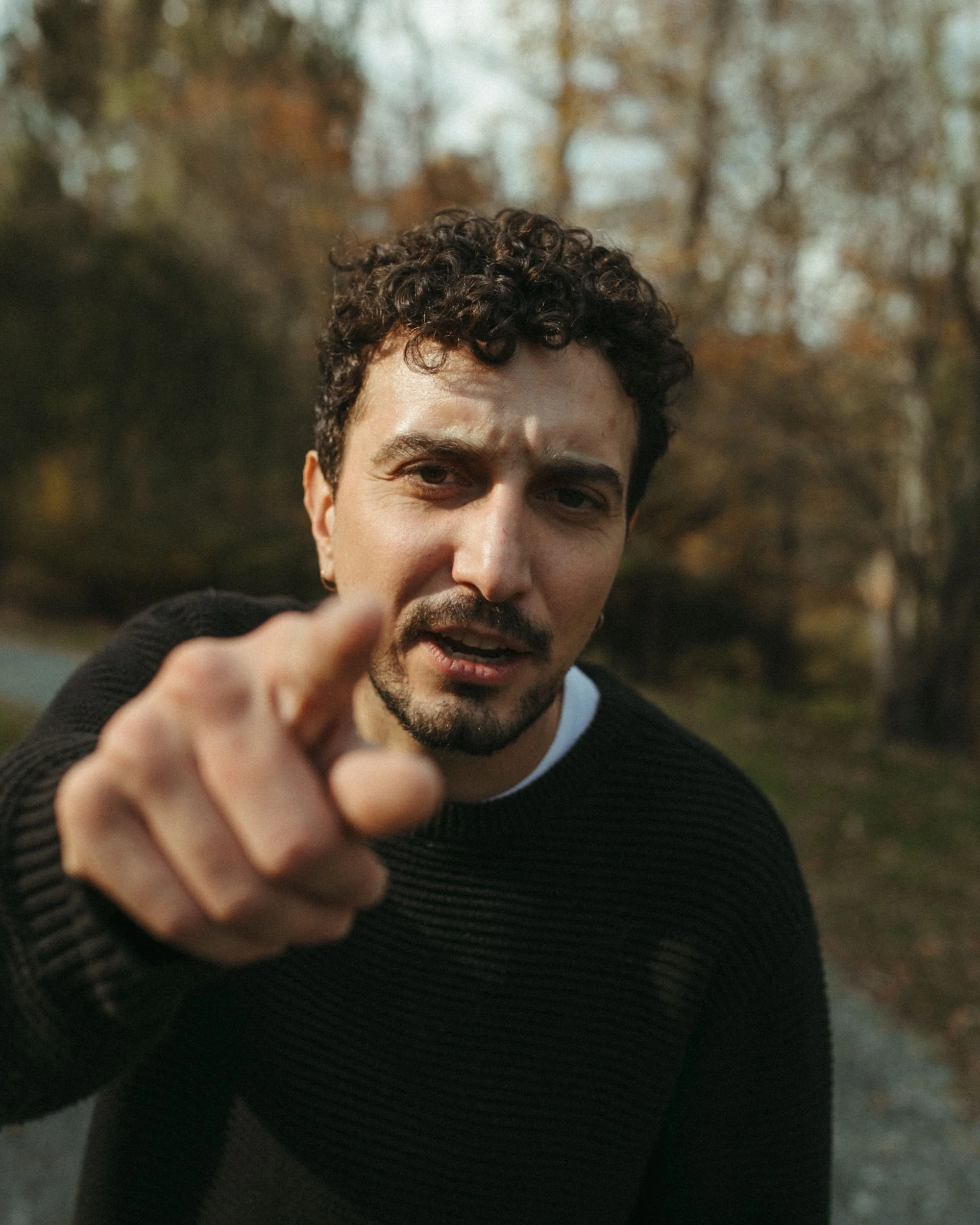 A Gilliam Writers Group faculty member points toward the camera amid blurred autumn trees.