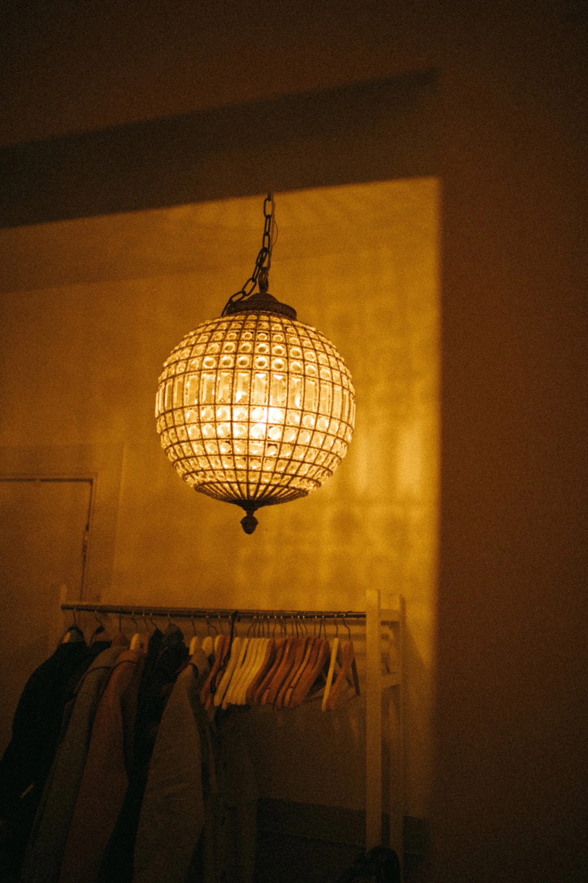 A glowing beaded-glass globe chandelier above a coat rack, setting the mood.