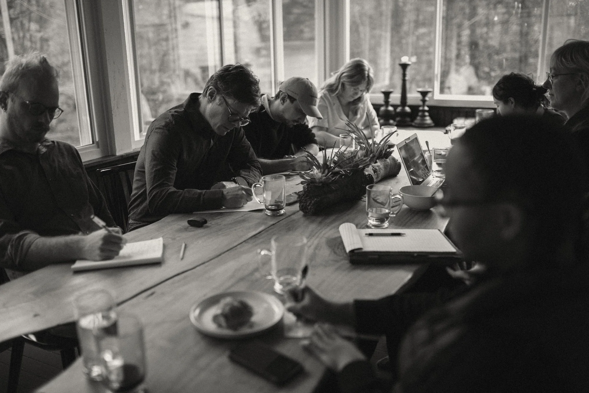 A GWG writing coach drafting by hand while colleagues type and work nearby.