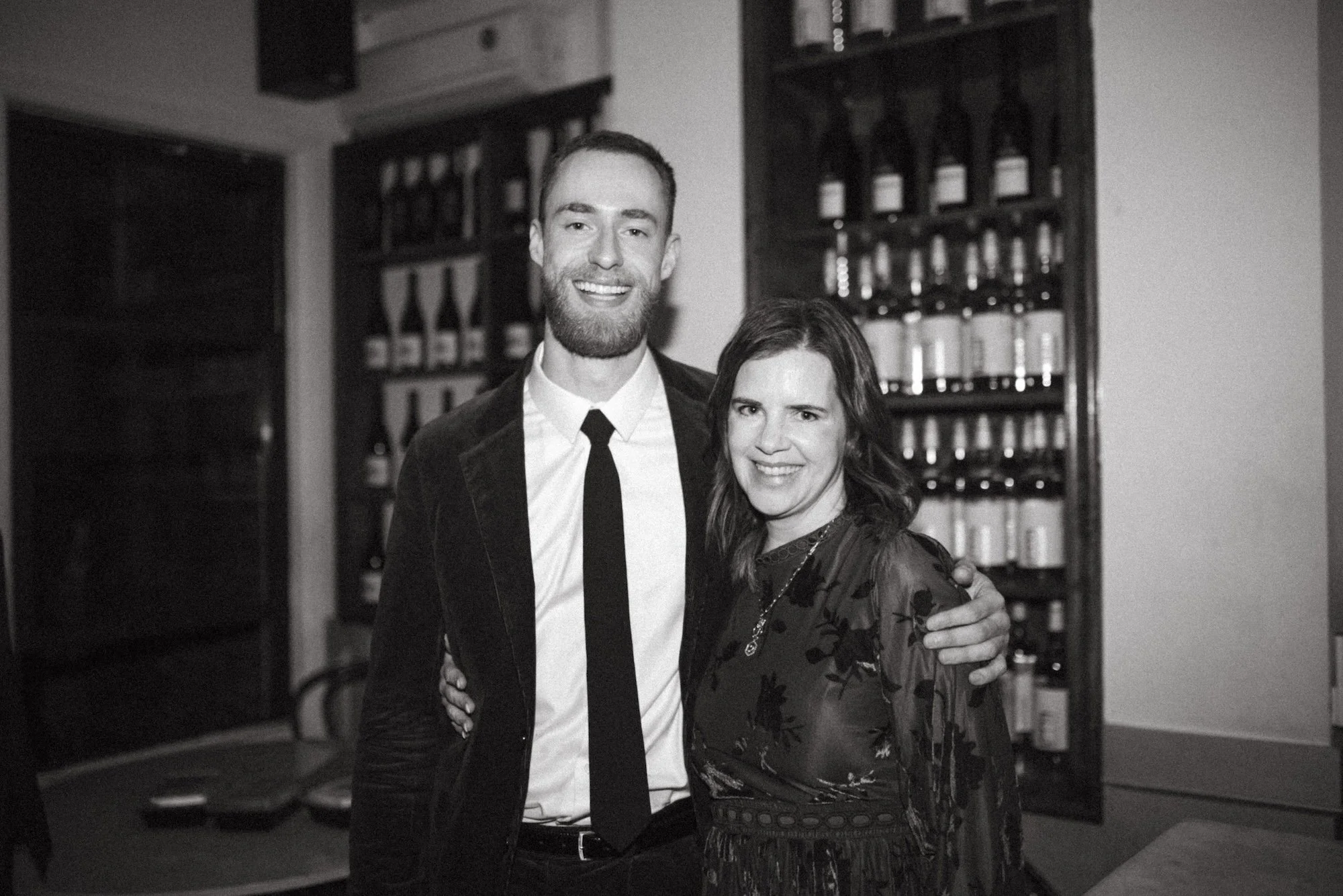Brady Gilliam and colleague smiling before a wall of wine bottles.