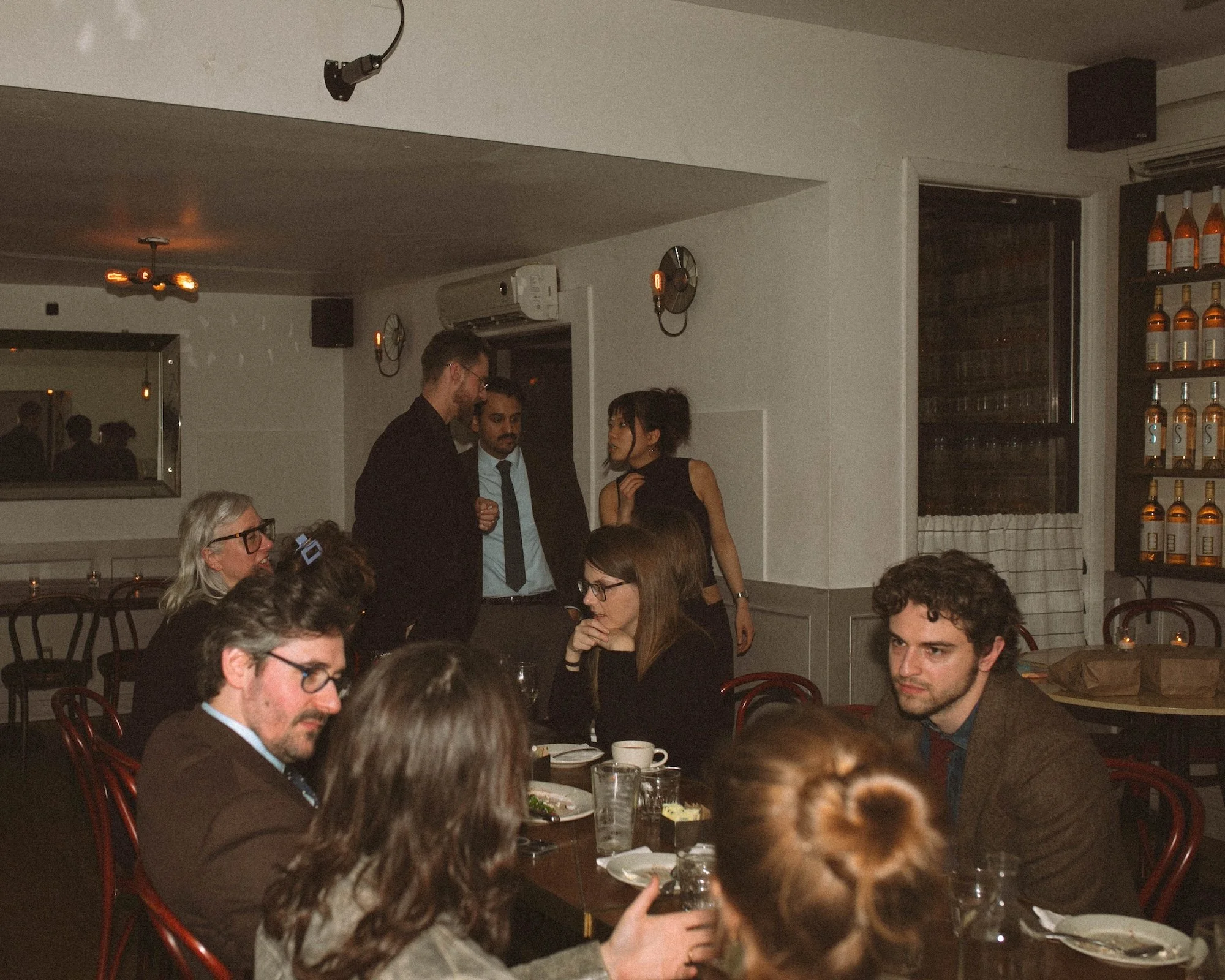 GWG faculty and visiting writers mingling and talking across a crowded evening dinner room.