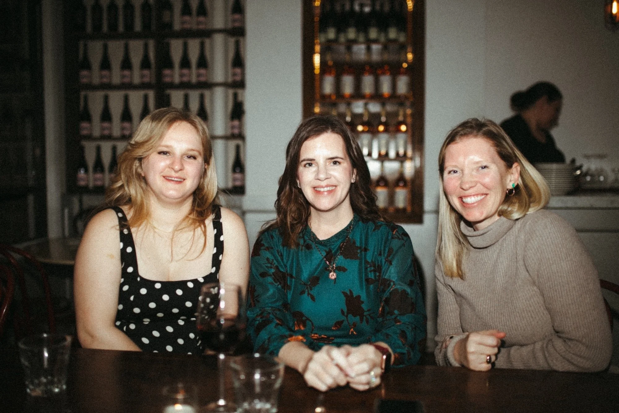A Gilliam faculty member and two guests smiling together before a restaurant's wine display.