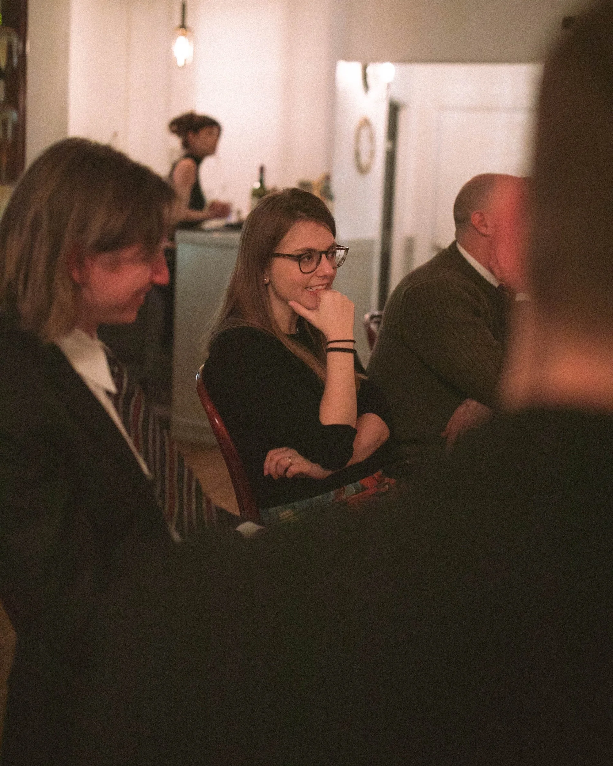 A faculty member smiling in conversation at a candlelit community dinner.