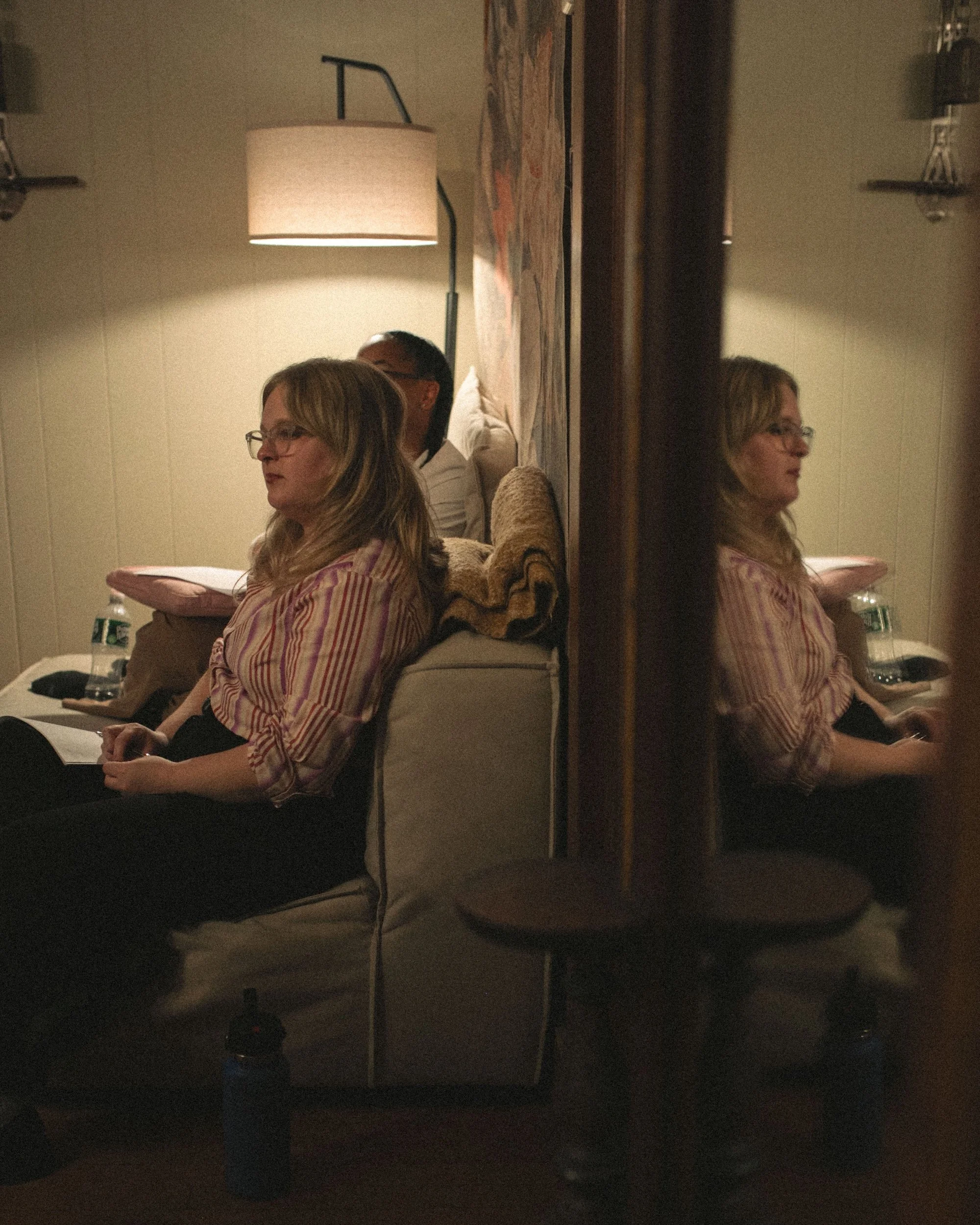 A writer taking notes during a retreat session, reflected in a mirror.