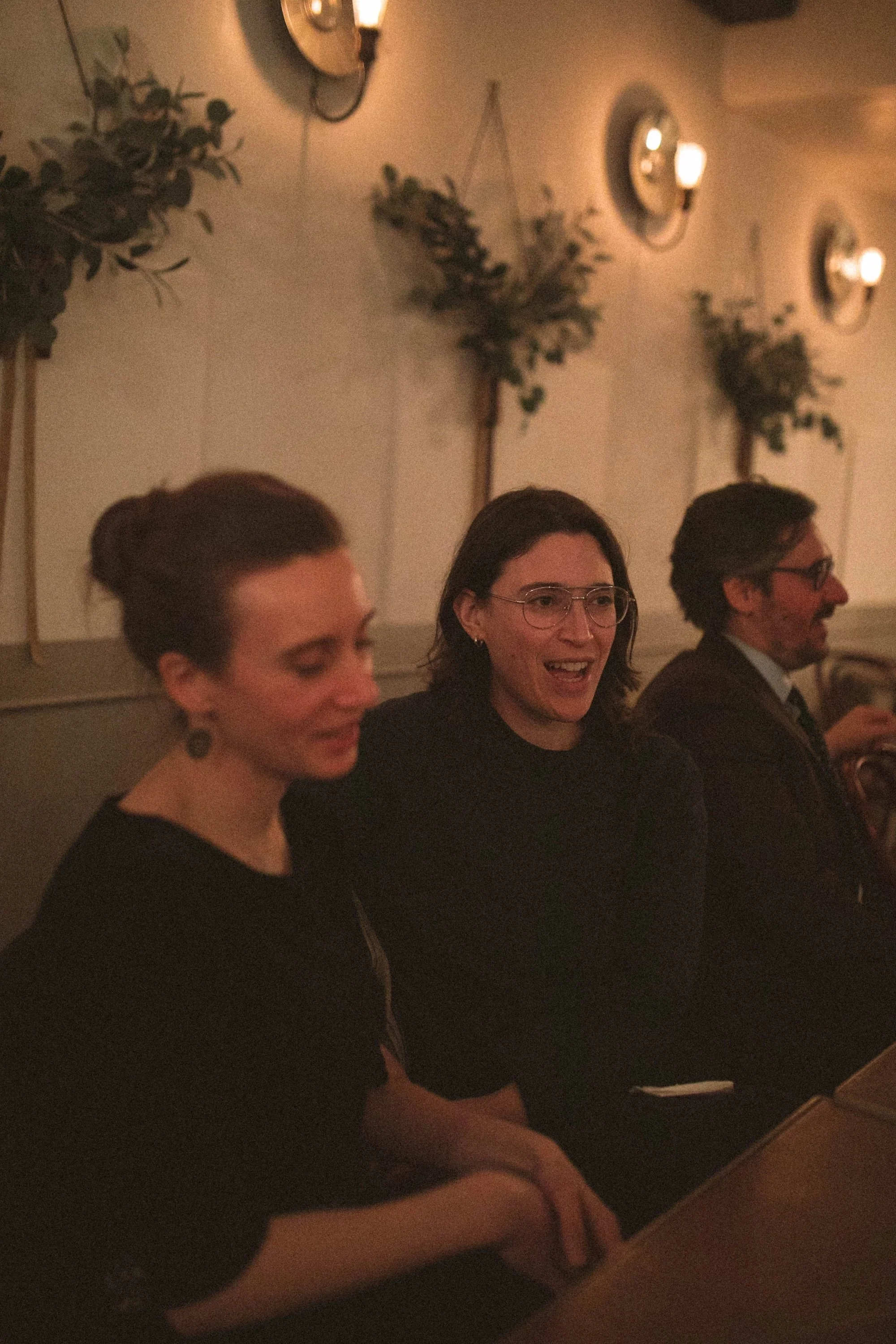 Two Gilliam Writers Group colleagues laughing together beneath greenery-draped wall sconces.