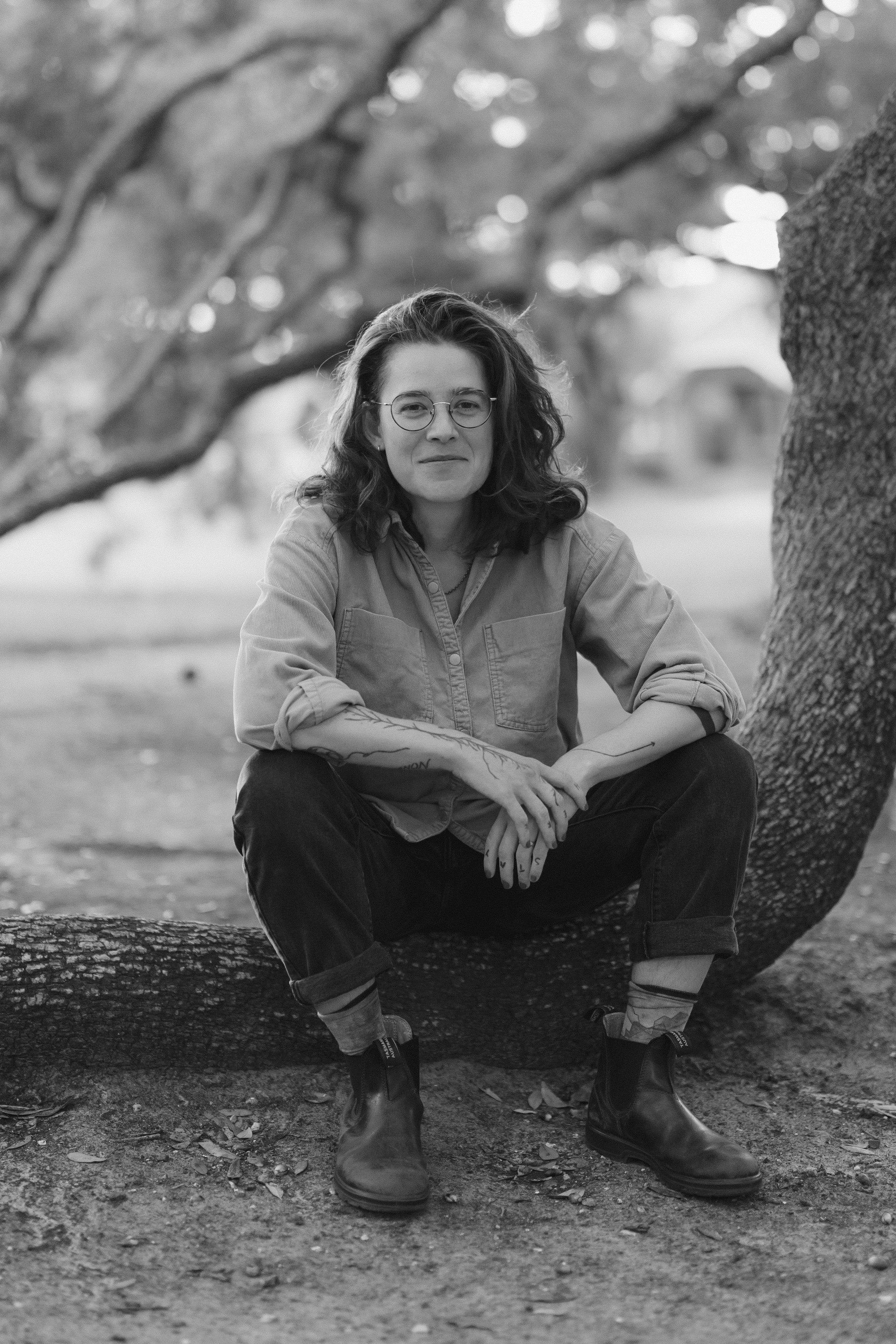 A Gilliam Writers Group faculty member sits on a low oak branch in dappled light.