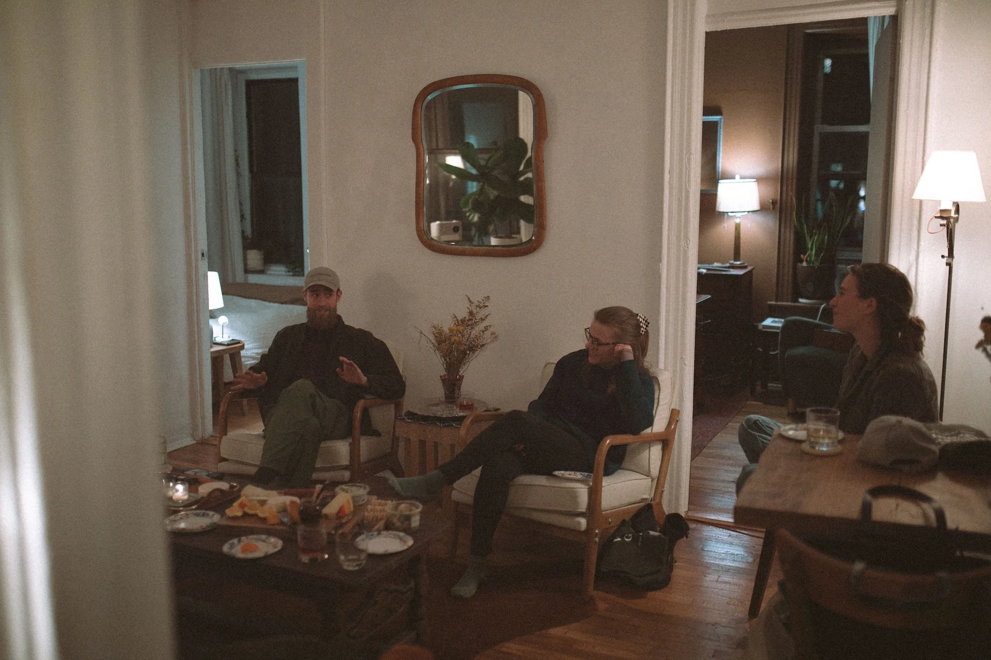 Brady Gilliam and two colleagues in relaxed conversation in a lamplit Brooklyn apartment.
