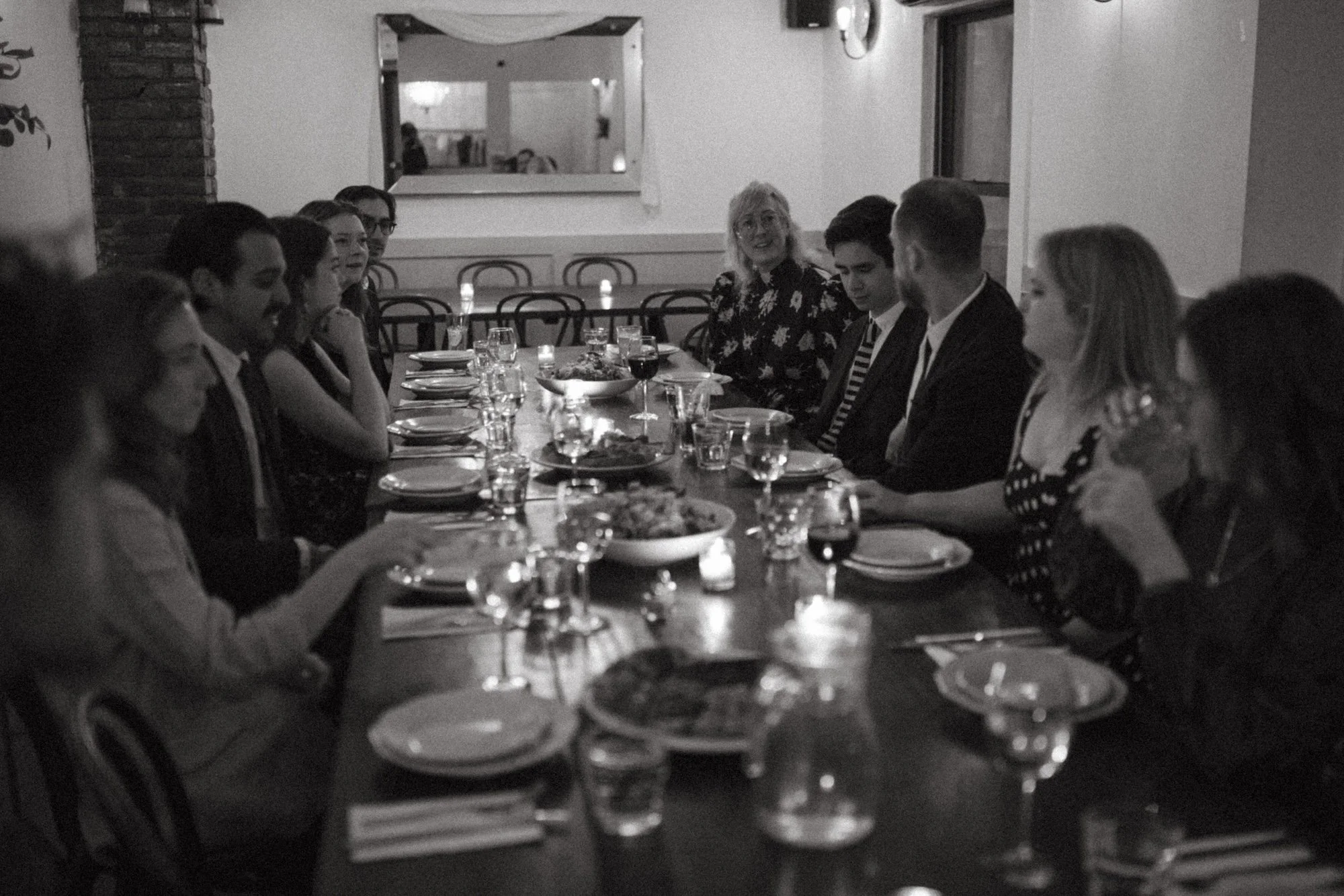 Faculty seated along a long candlelit table at a community dinner.