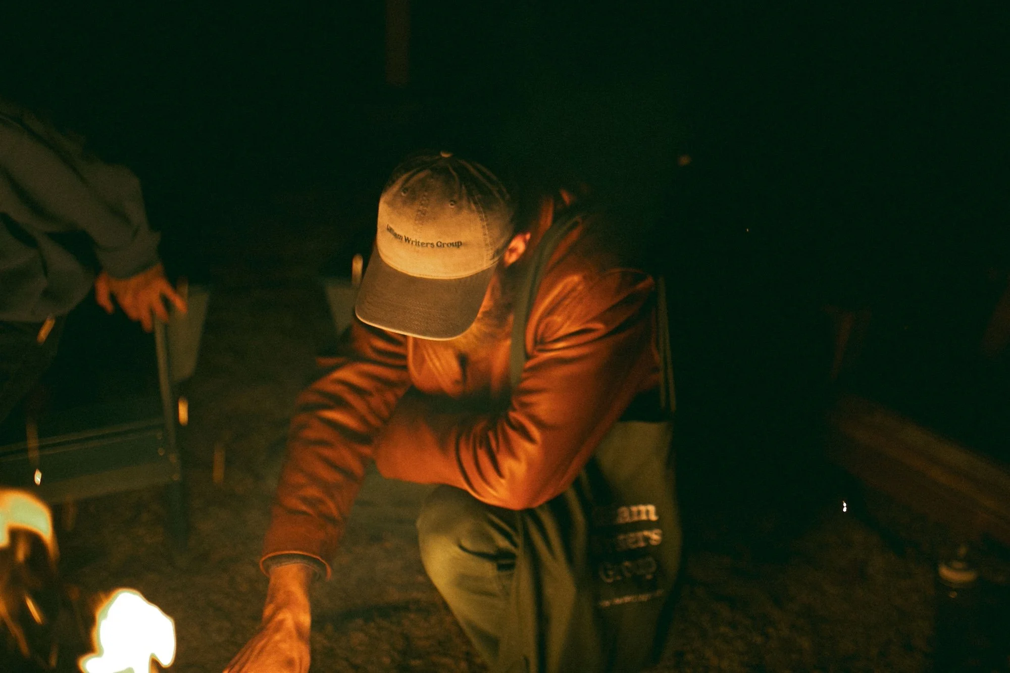 A faculty member in Gilliam Writers Group cap and leather jacket tends the fire.