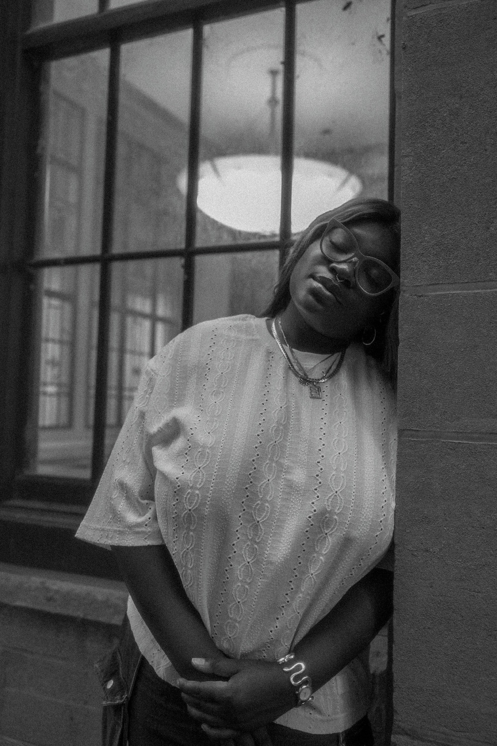 A writer in a white eyelet top leans against a column beside a tall window.