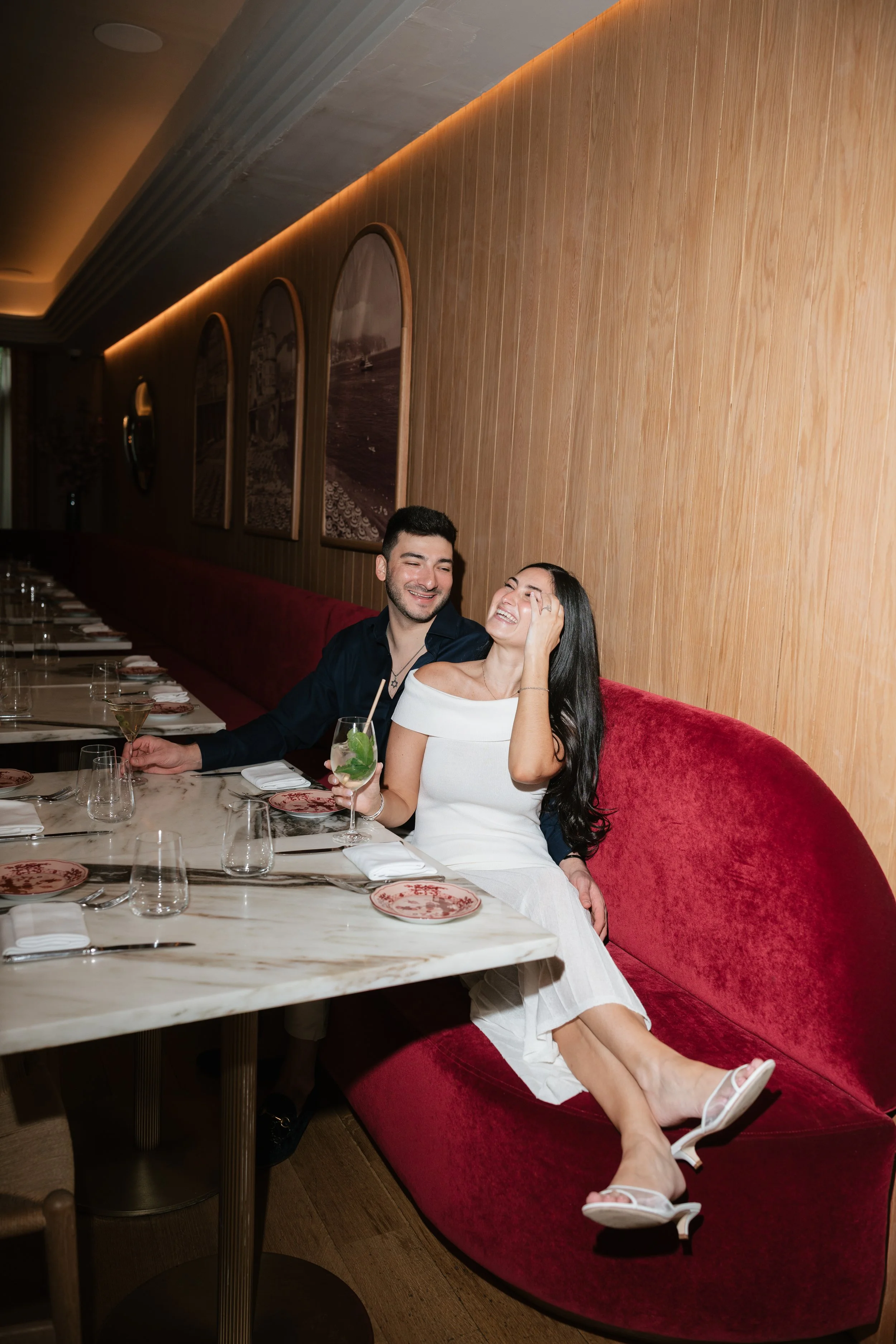 Couple laughing together over cocktails during an engagement session at a cozy Upper East Side restaurant in New York City.