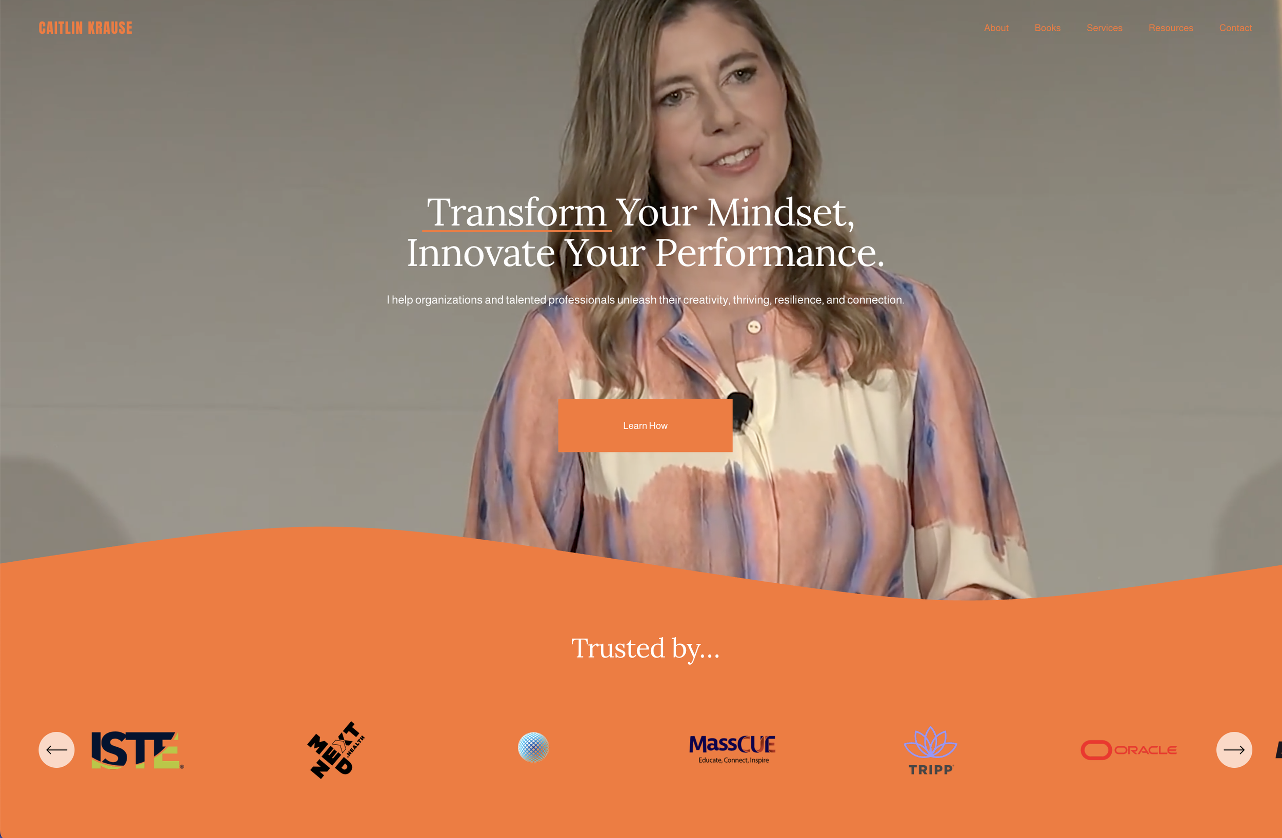 A woman with wavy, shoulder-length hair in a colorful, patterned blouse speaking on stage with a microphone. The webpage features a headline about transforming mindsets and improving performance, with a call-to-action button labeled "Learn How." The top menu includes links: About, Books, Services, Resources, Contact. The lower section displays logos of various organizations against an orange background.