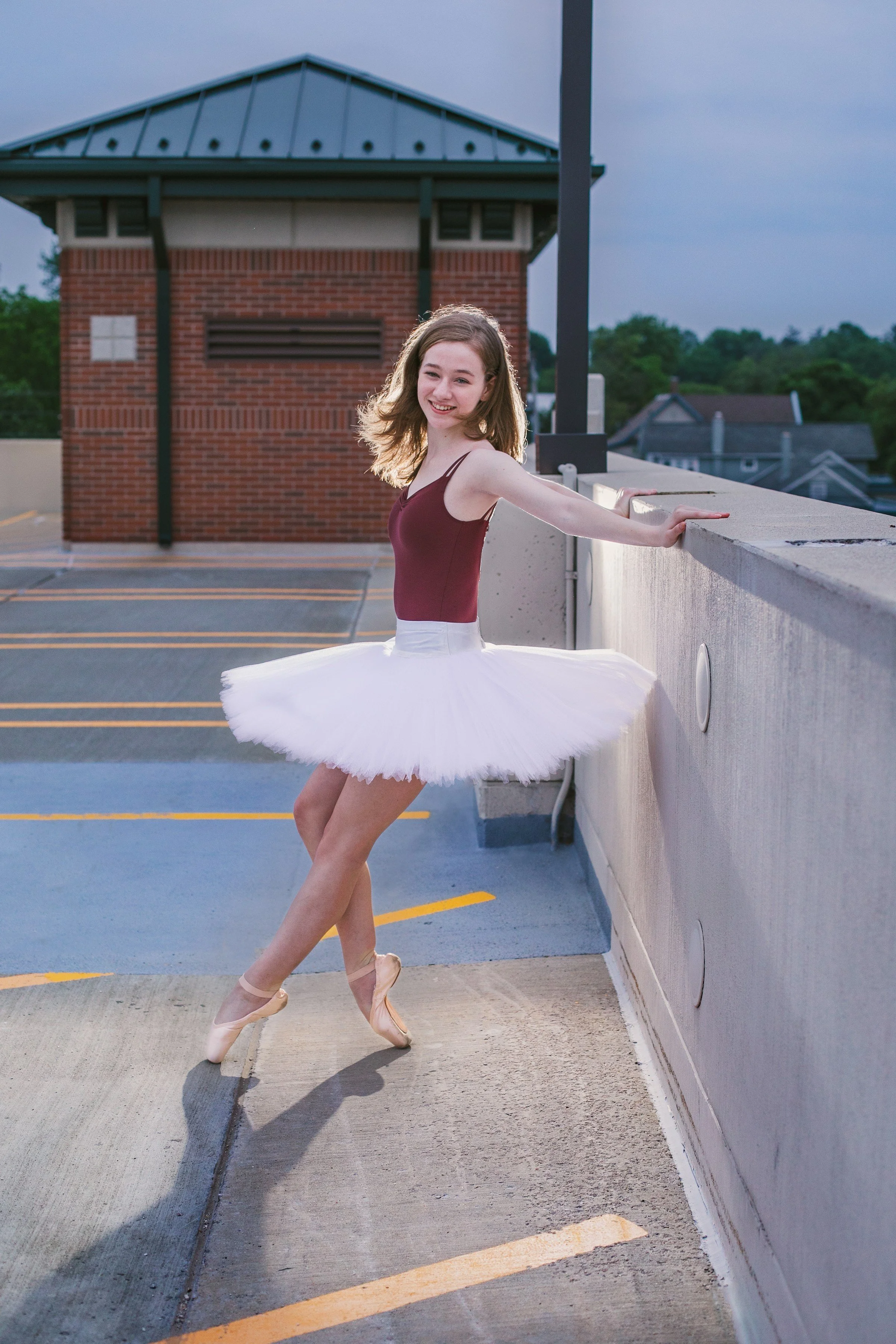 Young girl in a ballet tutu and pointe shoes dancing on a parking garage rooftop.