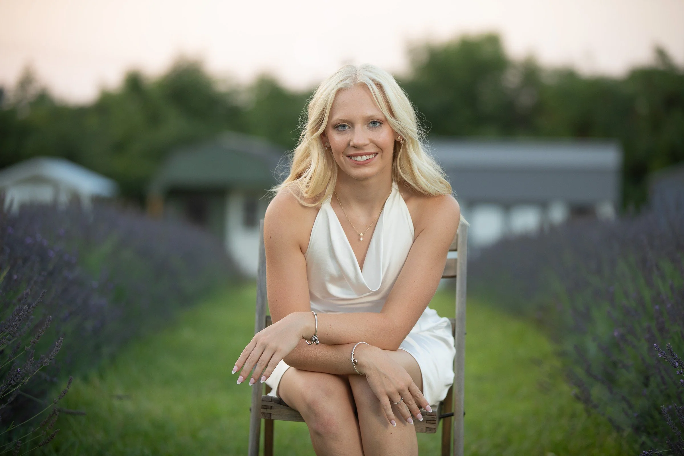 A woman with blonde hair in a white dress sitting outdoors with lavender plants in the background.