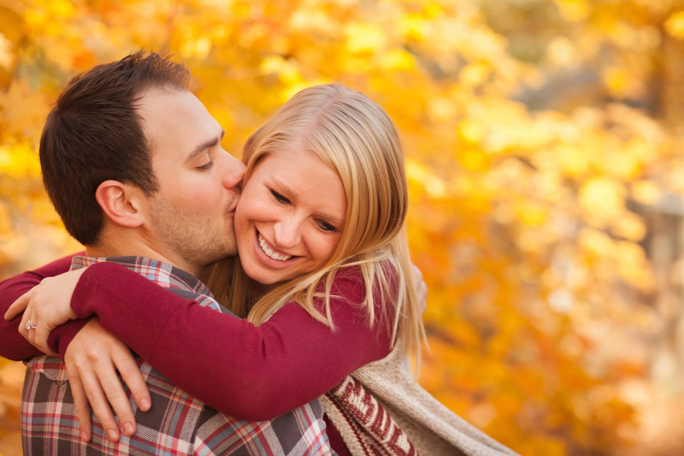 A couple hugging outdoors with fall foliage in the background.