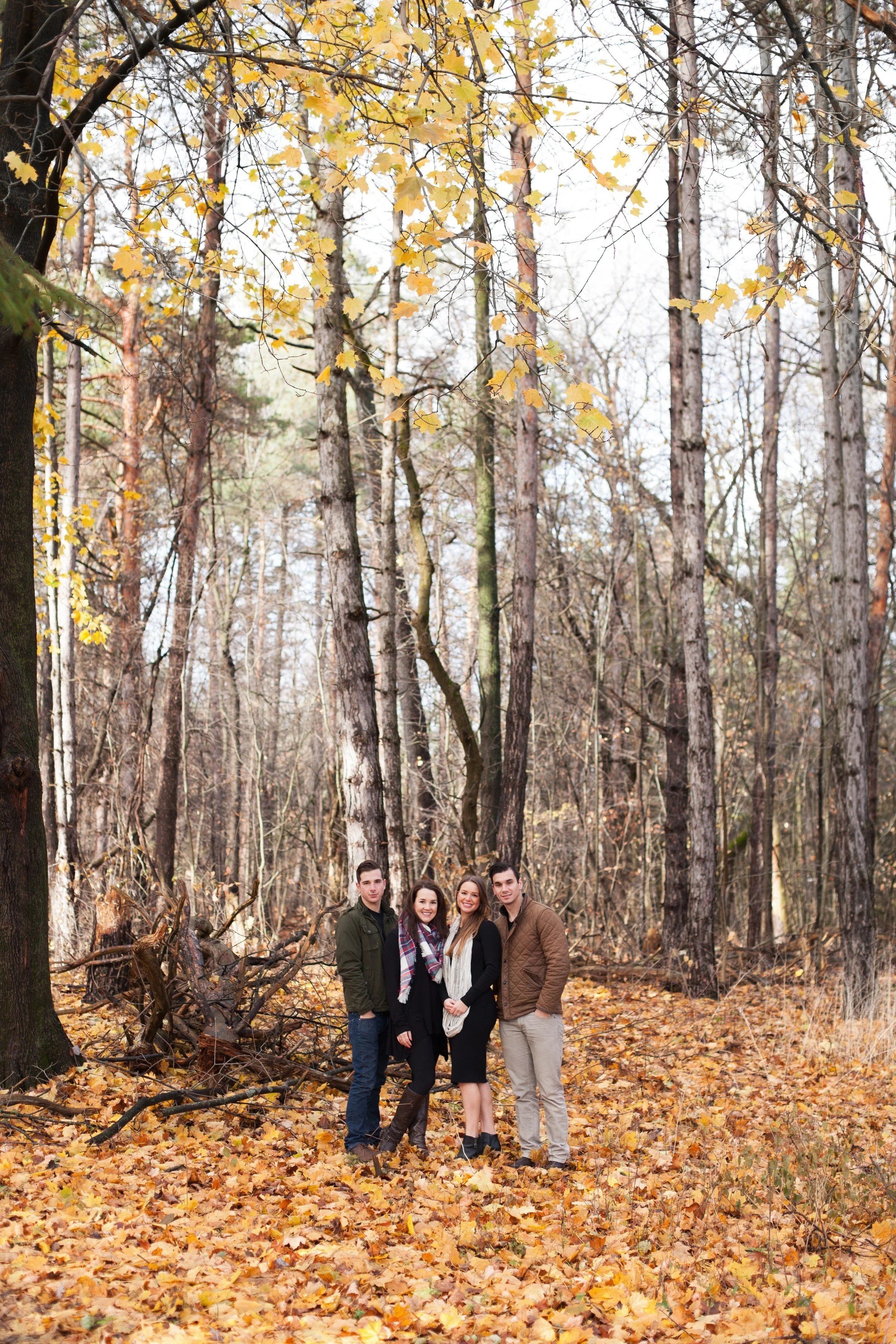 Four people standing together in a forest during autumn, with yellow leaves on trees and on the ground.