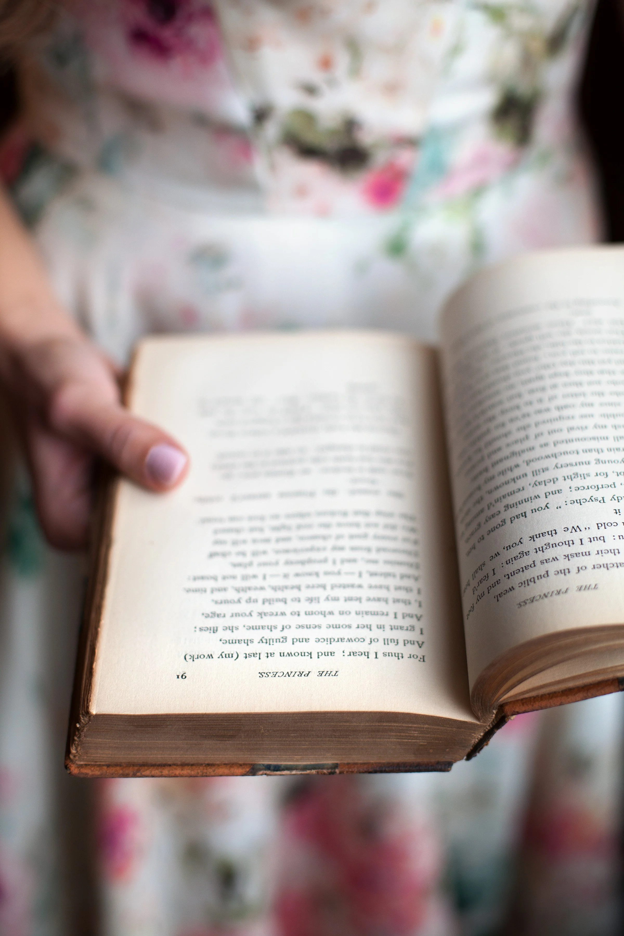 A person holding an open book, with the focus on the pages and hand, while the background is blurred.