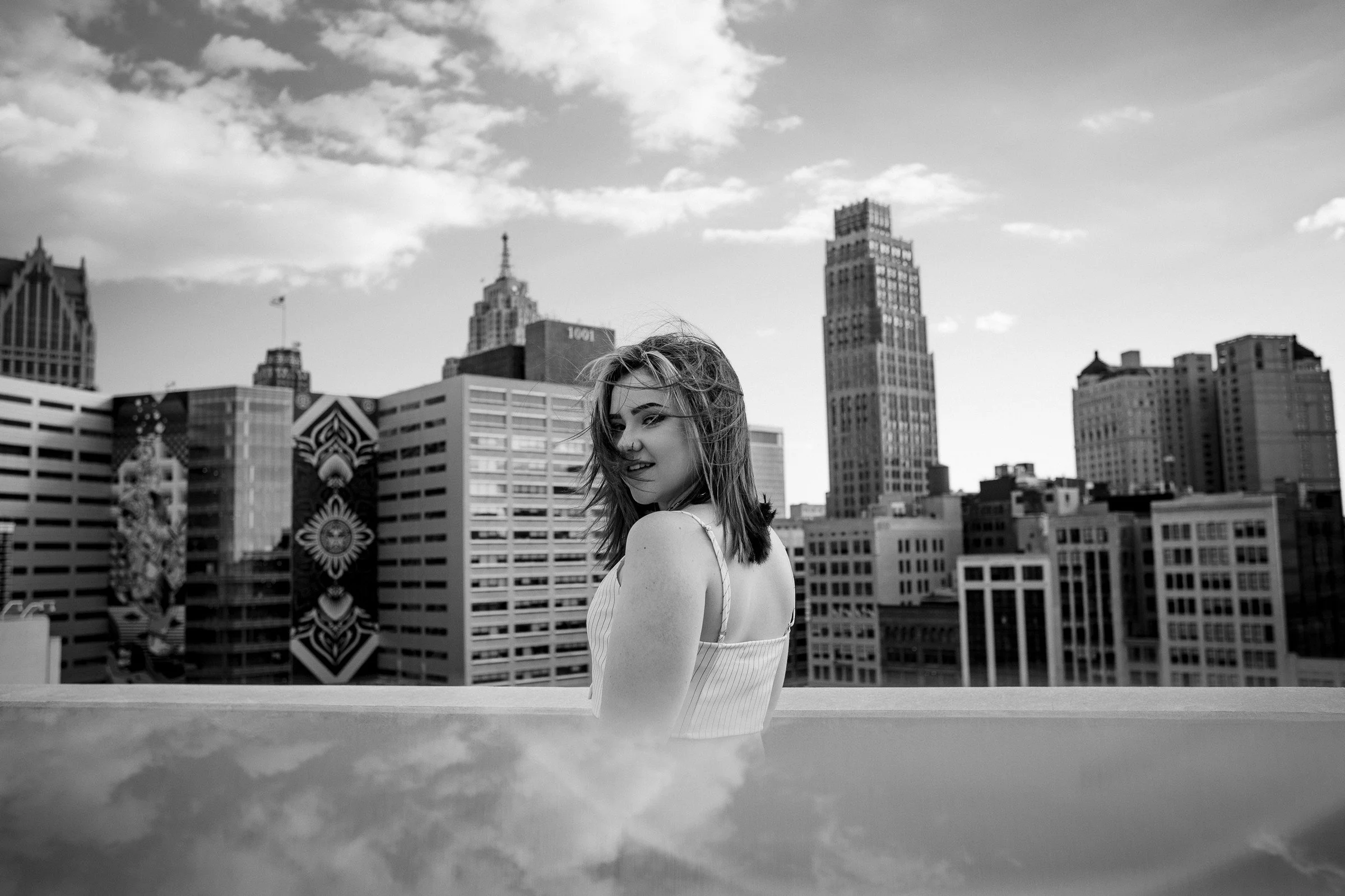 A woman standing on a rooftop with a city skyline in the background, black and white photo.