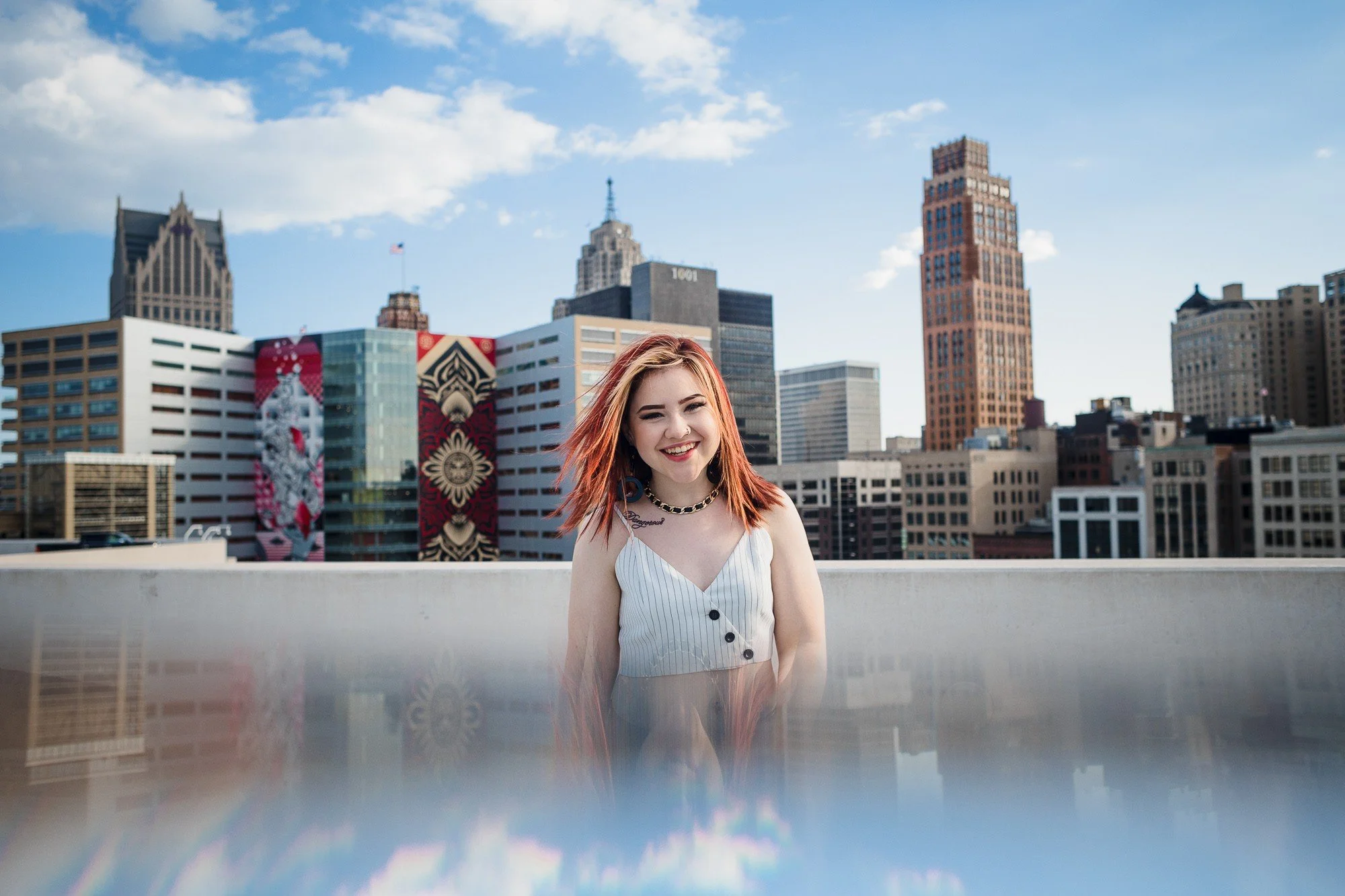 Young woman with red hair smiling on a rooftop with a city skyline background.