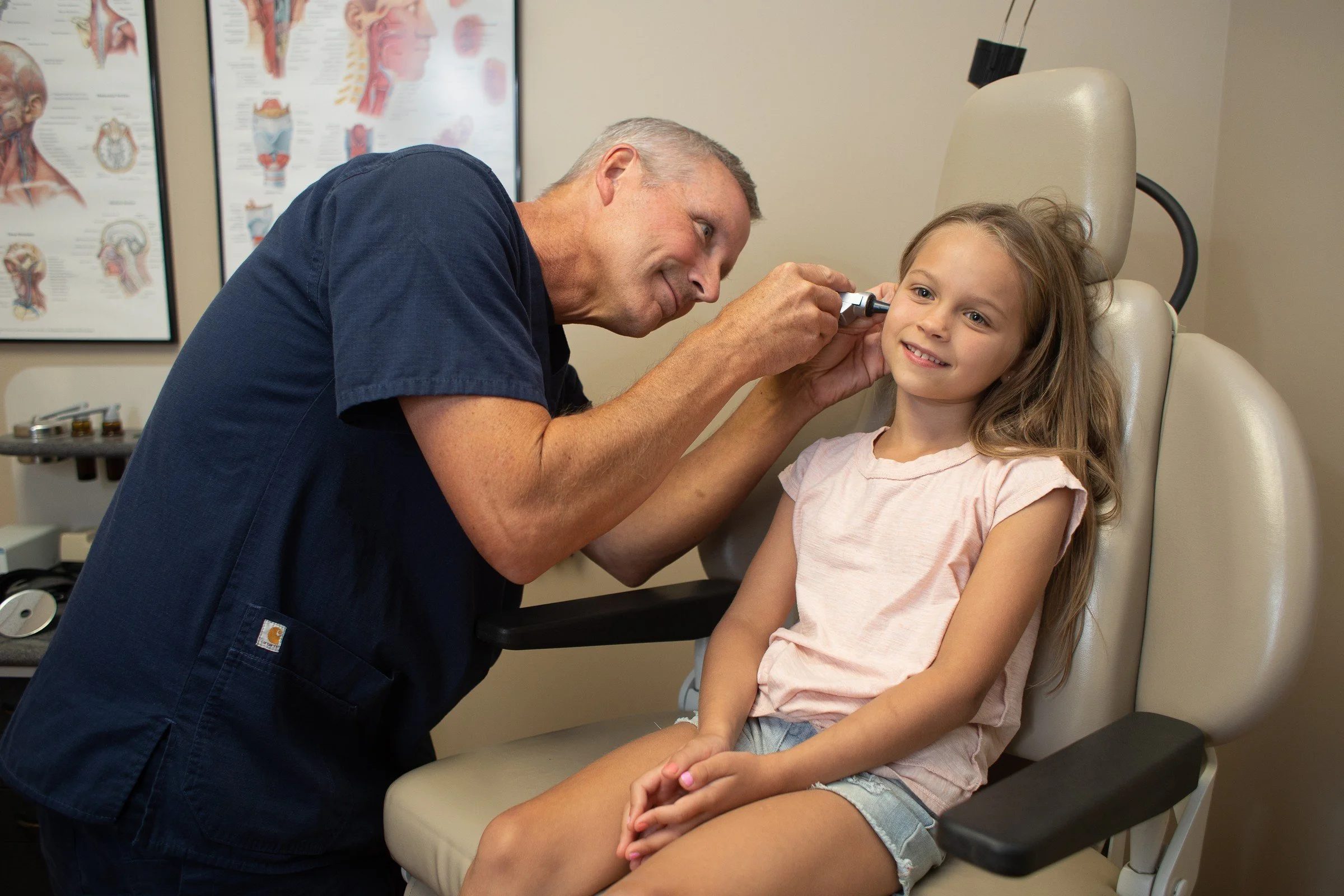 A doctor examines a young girl with an otoscope in a medical office.