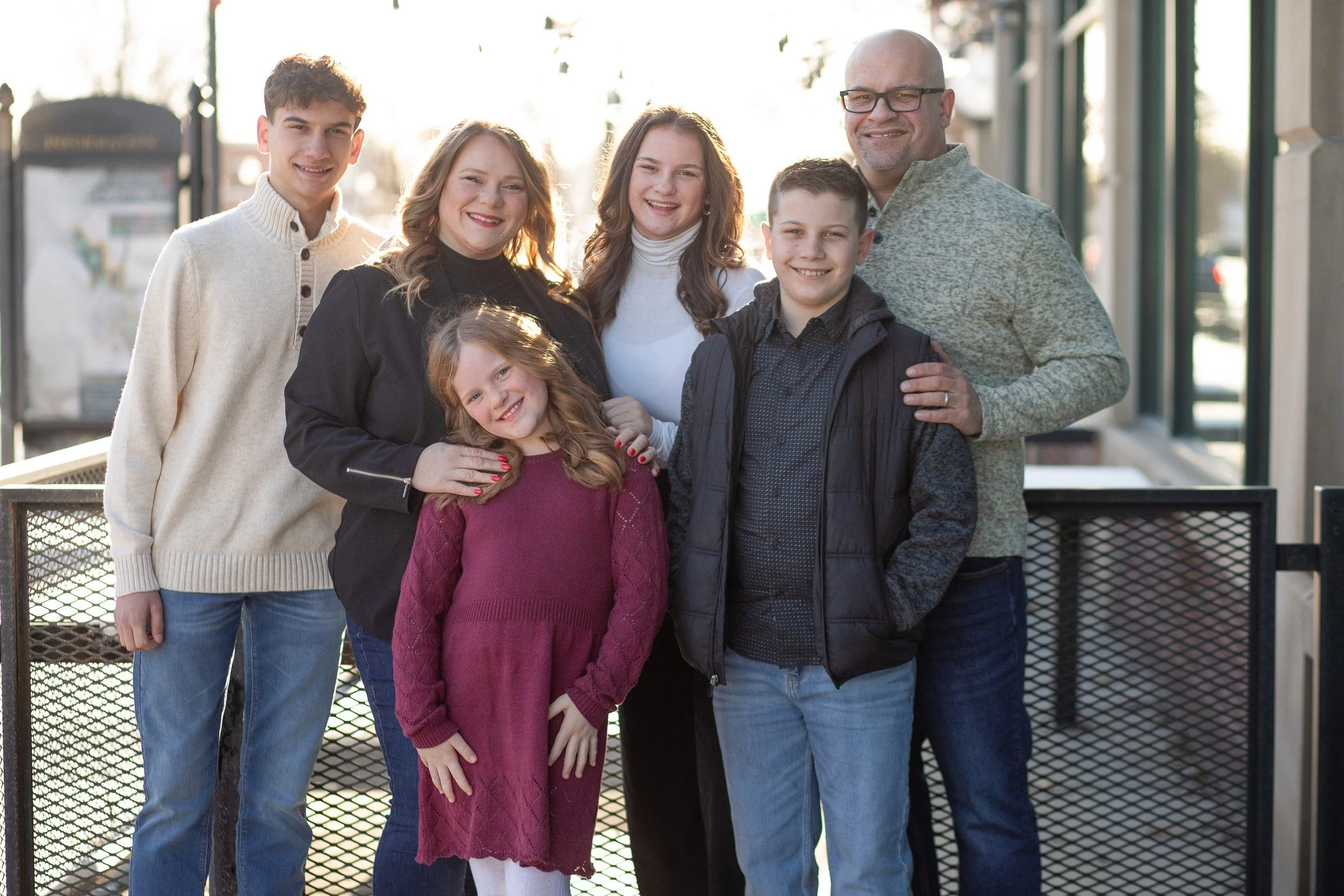 A family of seven, including three children, standing together outdoors near a building with large windows, smiling at the camera.