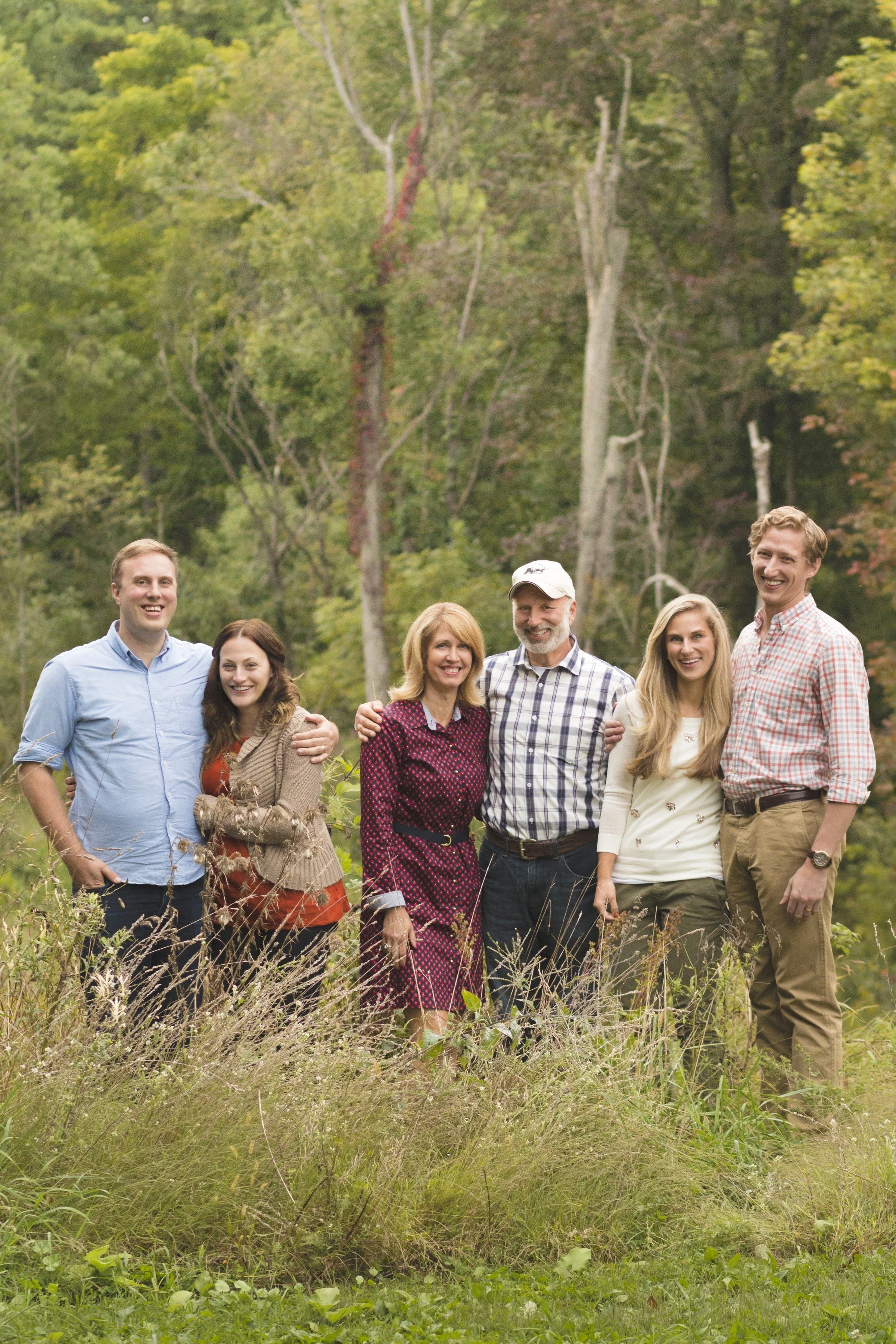 A group of six people standing outdoors in a grassy area with trees in the background, smiling and posing for a photo.