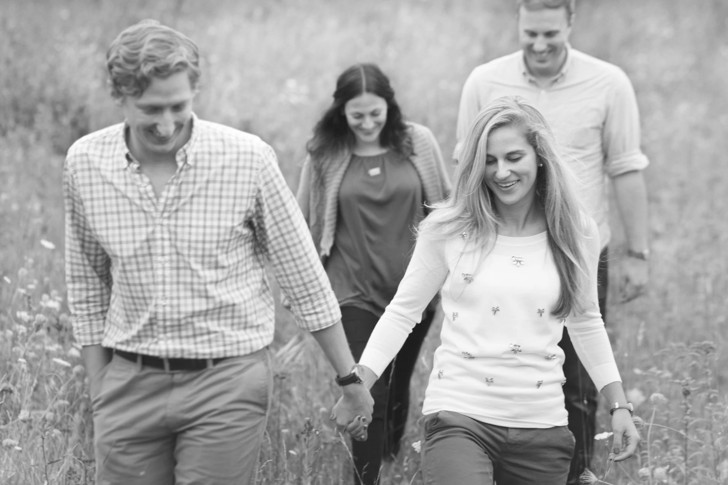 A group of five friends walking outdoors in a grassy field, holding hands and smiling.