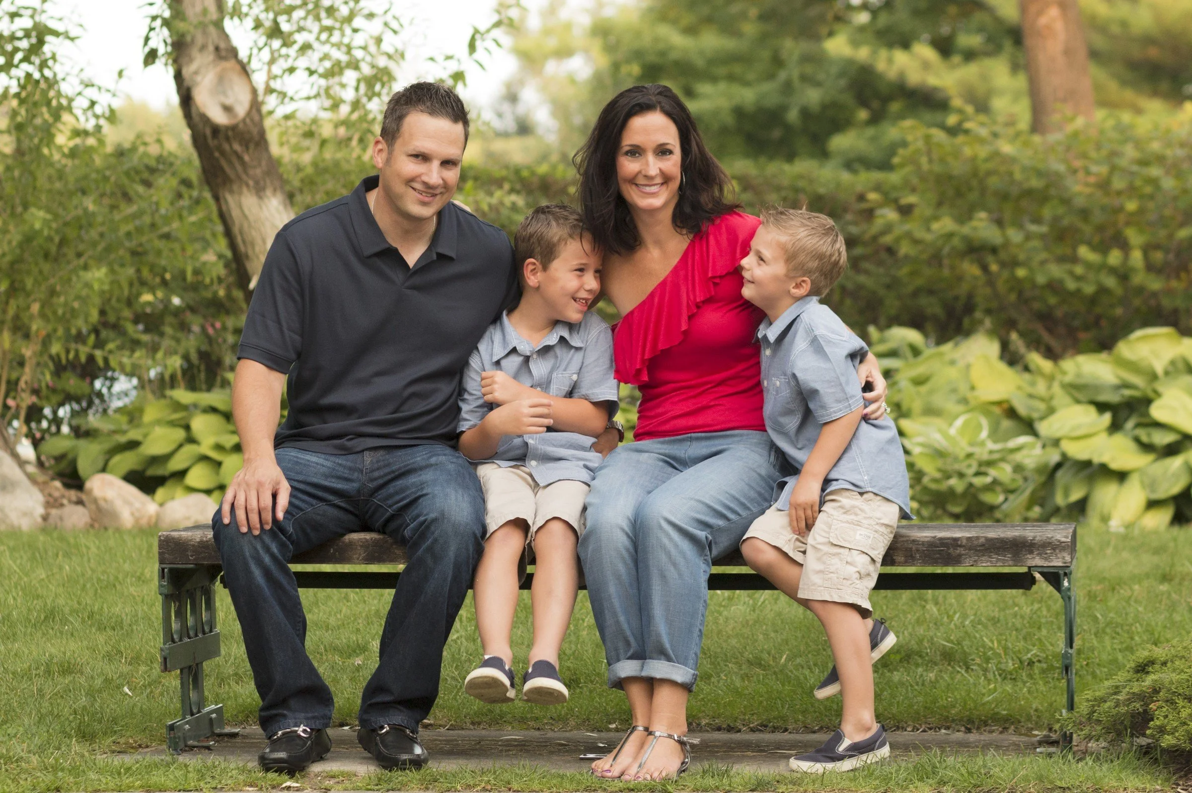 Family of four sitting on a park bench, smiling and enjoying time together outdoors.