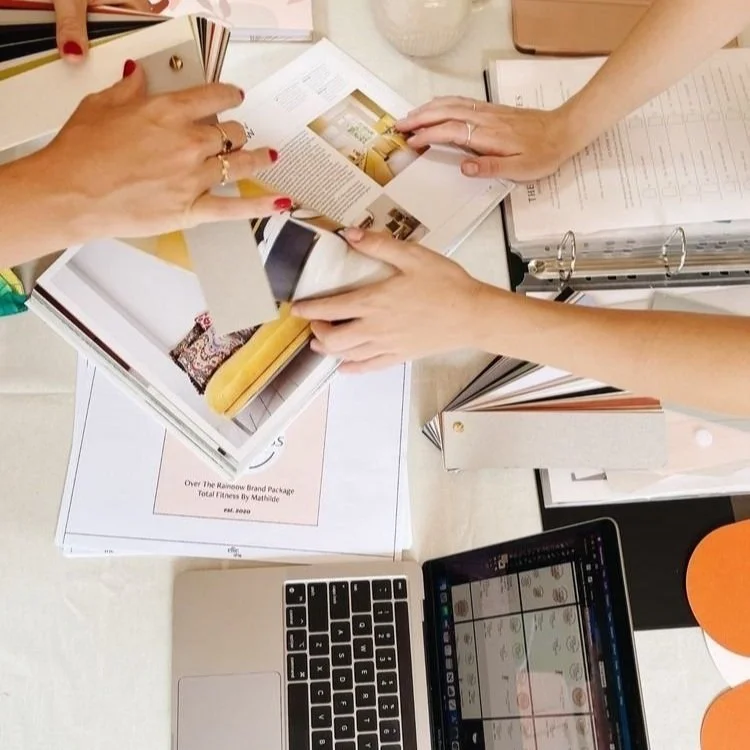 Creative formatting. Image behind the scenes, interacting over design materials and a laptop, with color swatches, brochures, and a binder on a table.