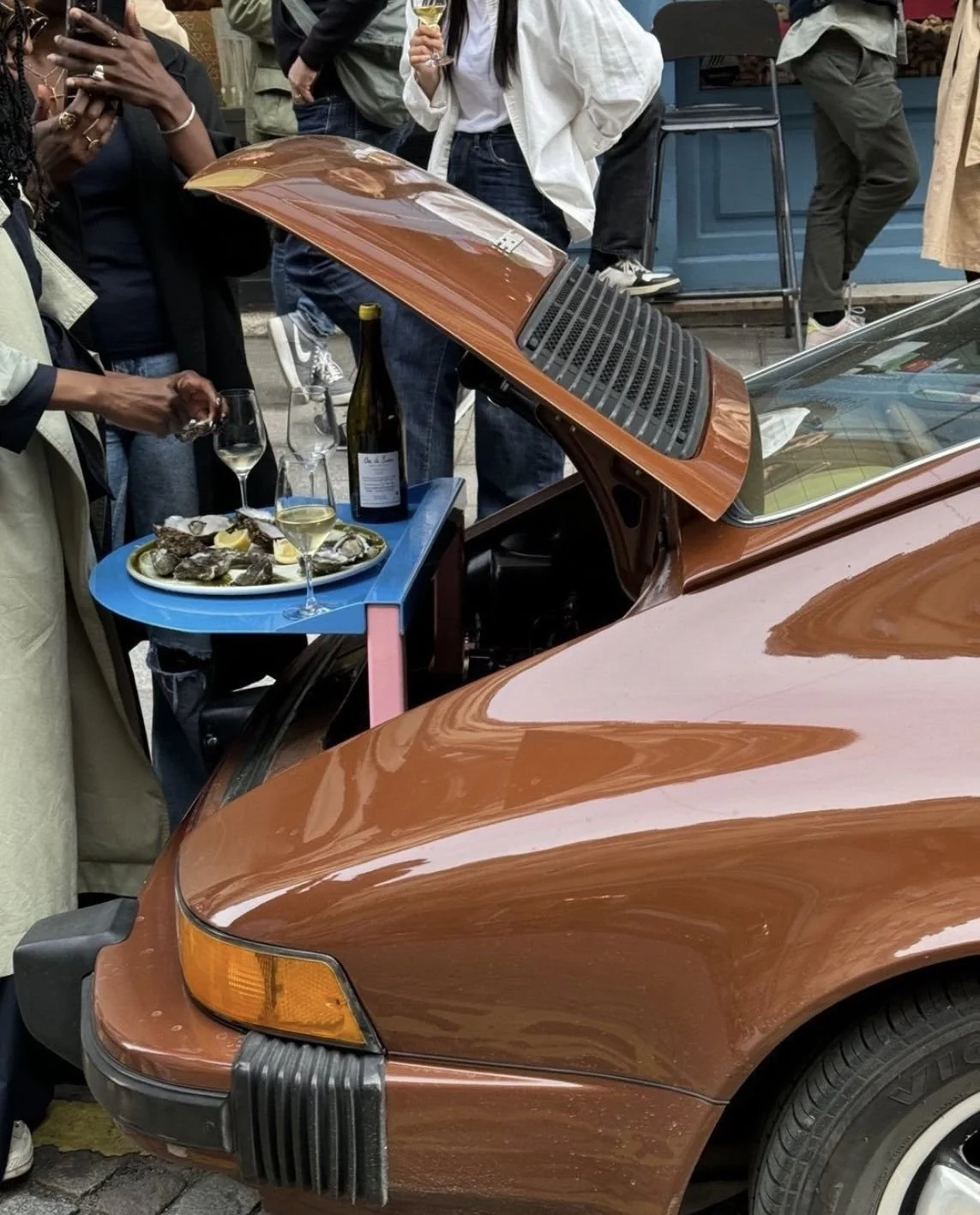 People descriptions (various): Portrait of individuals in lifestyle settings. Creative lifestyle and micro-trend scene; vintage Porsche as a makeshift table holding a platter of oysters and champagne.