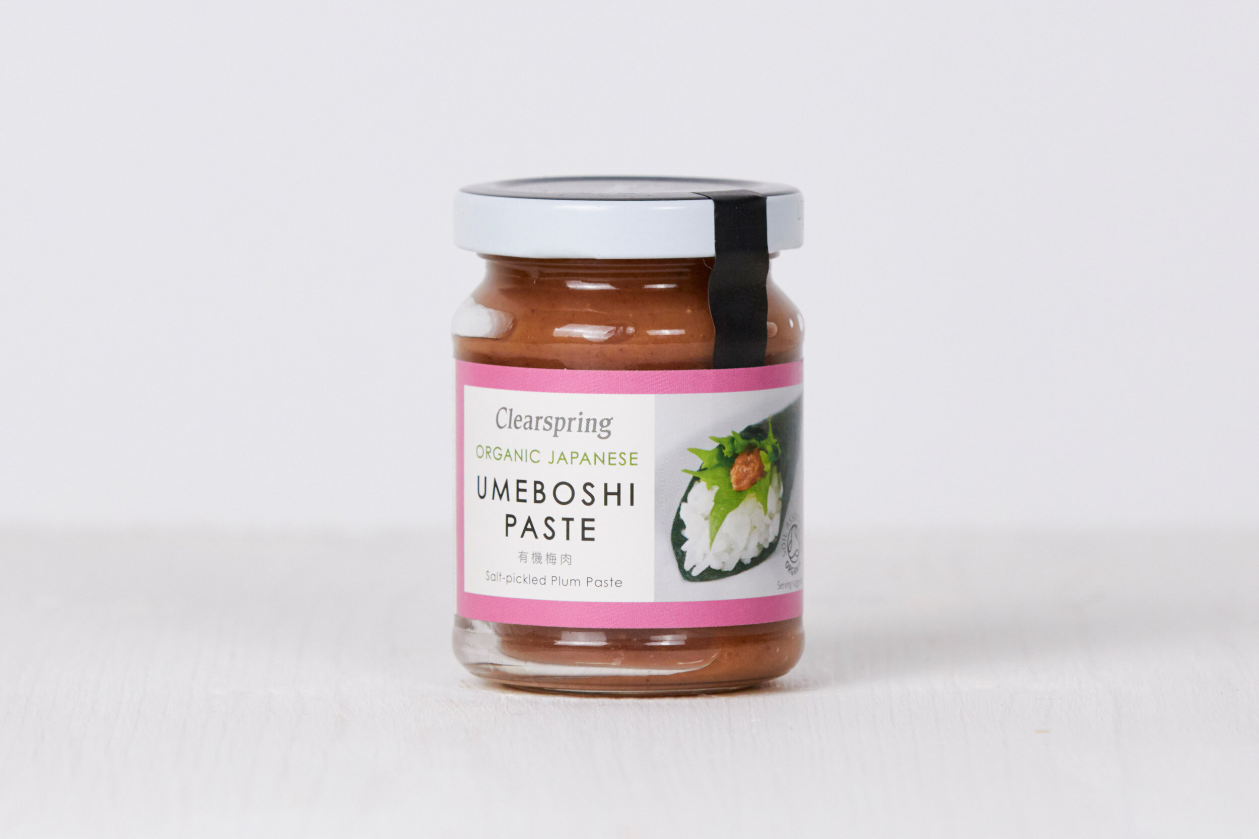 A jar of Clearspring Umeboshi Paste with a pink and white label, featuring an image of a rice ball with umeboshi on top, placed on a white surface against a plain background.